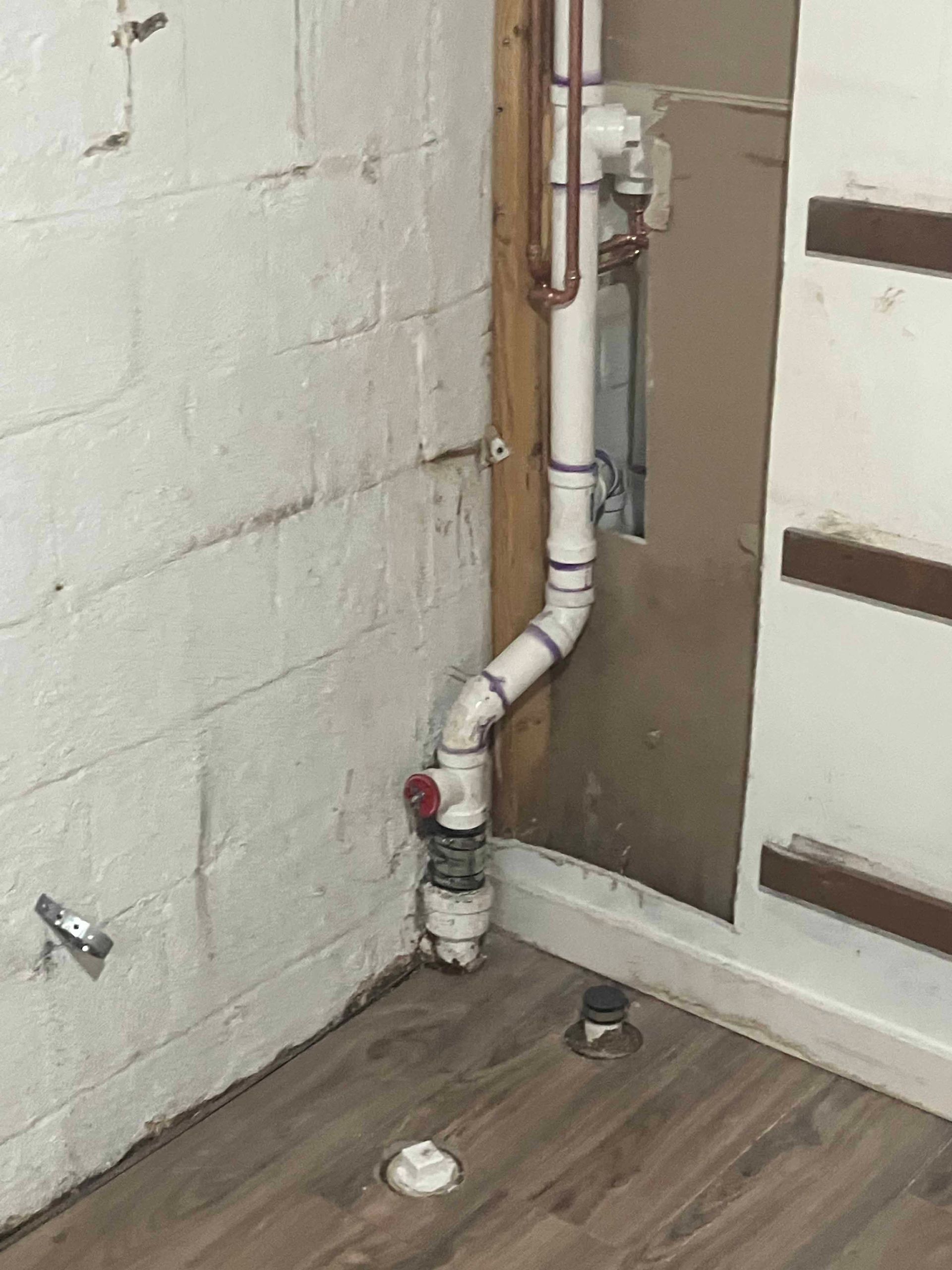 A white pipe is connected to a brick wall in a basement.
