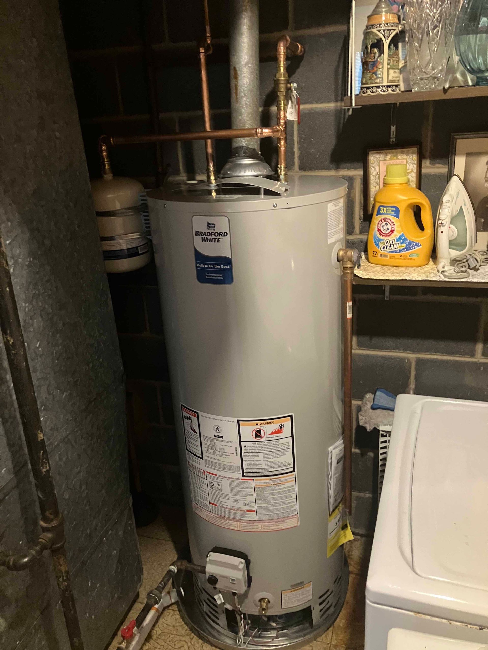 A water heater is sitting in a laundry room next to a washer and dryer.