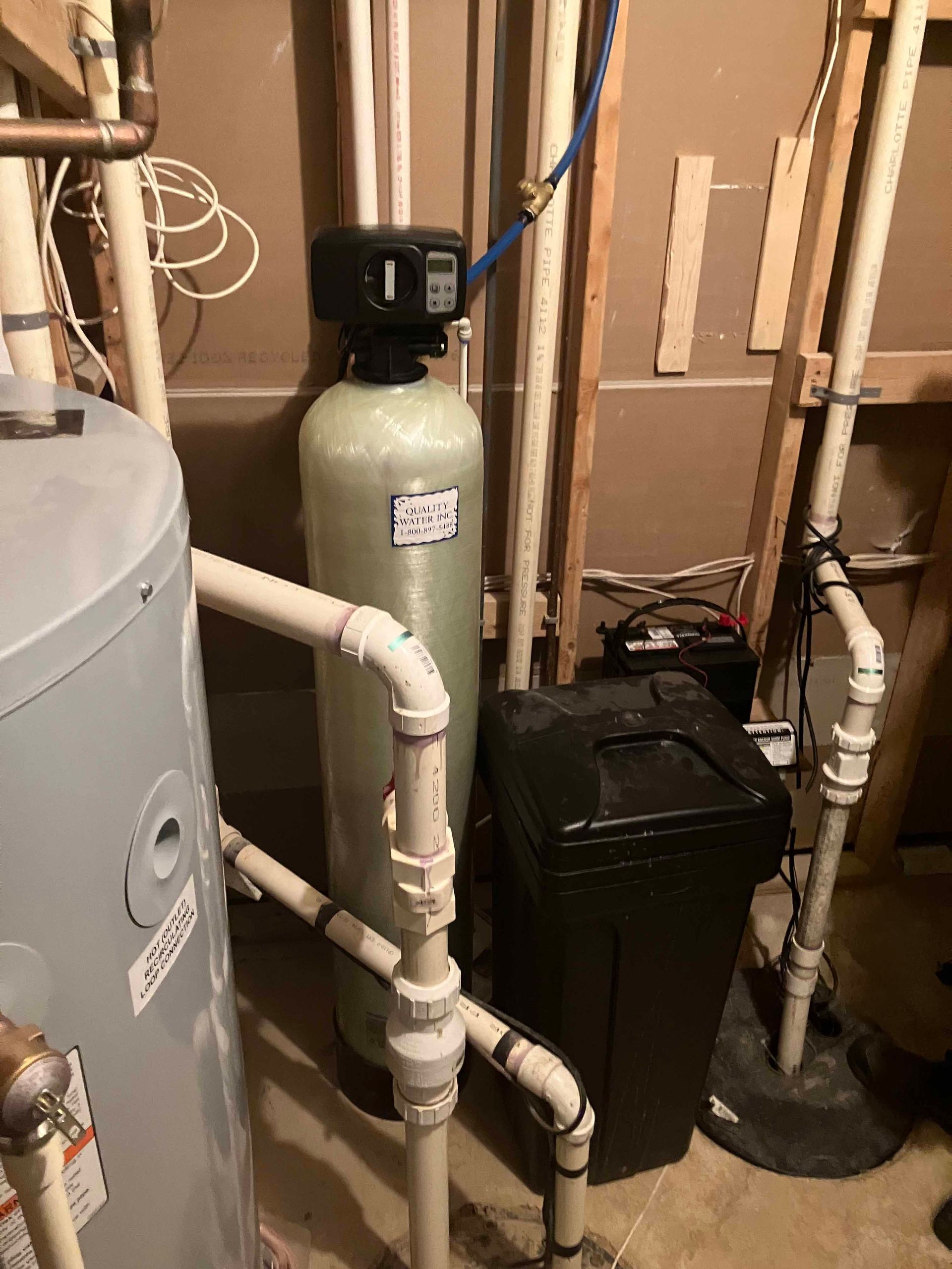 A water filter is sitting next to a water heater in a basement.