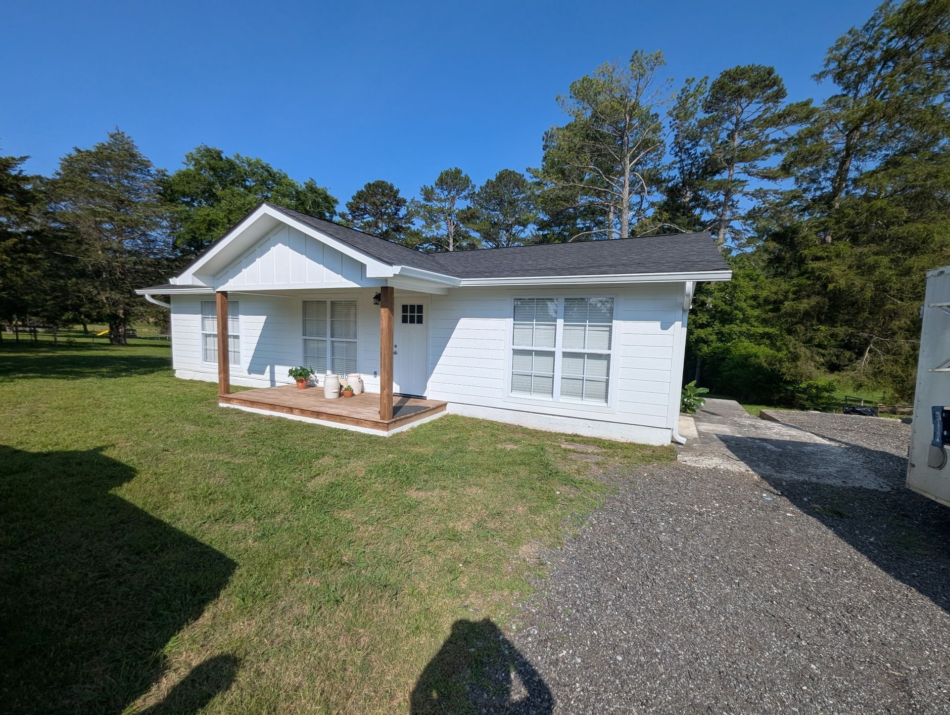 A small white house with a porch and trees in the background