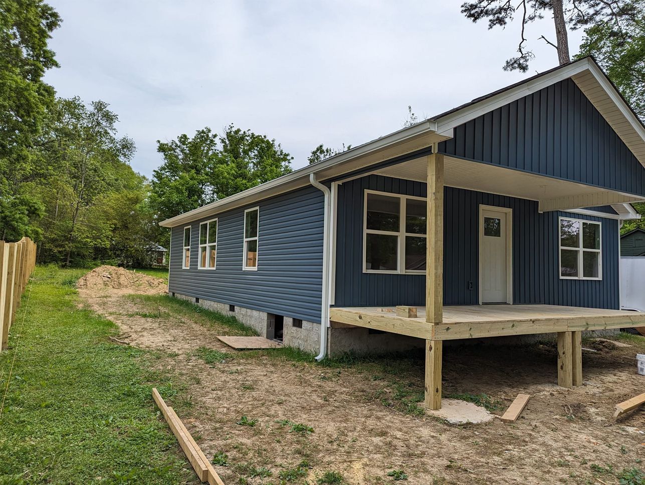 A blue house with a porch and a wooden deck is being built.