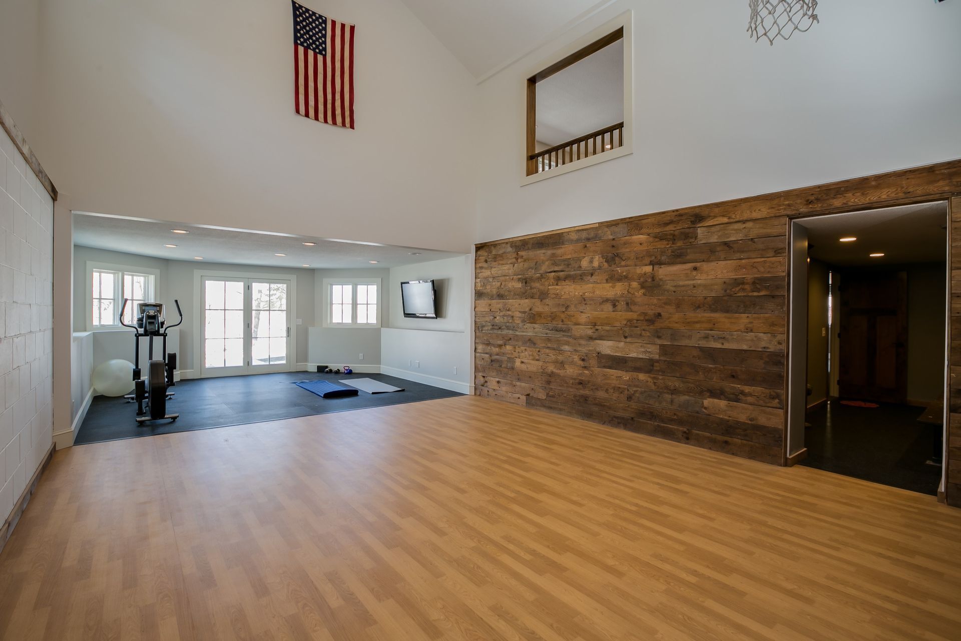 A large empty room with a wooden floor and an american flag hanging from the ceiling