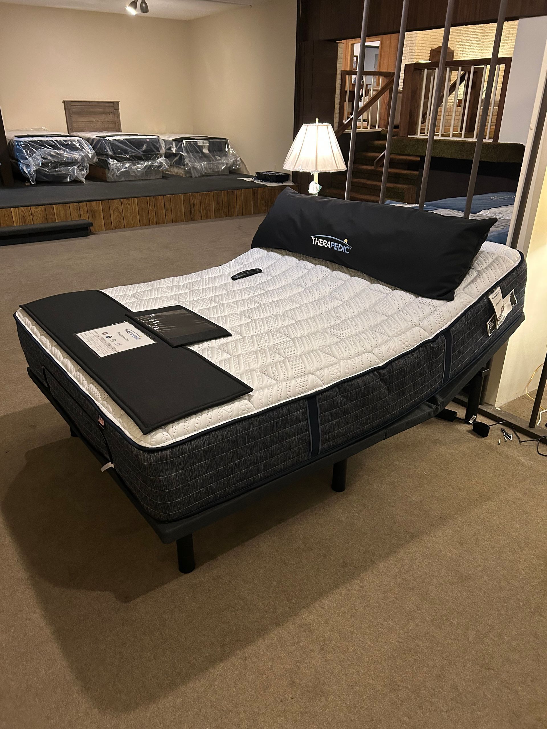 Adjustable bed with mattress in a showroom. It has a black headrest, control tablet, and is set up at an angle.