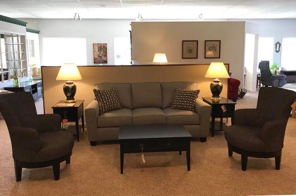 Living room furniture display: gray sofa, patterned armchairs, black coffee table, lamps, and art.