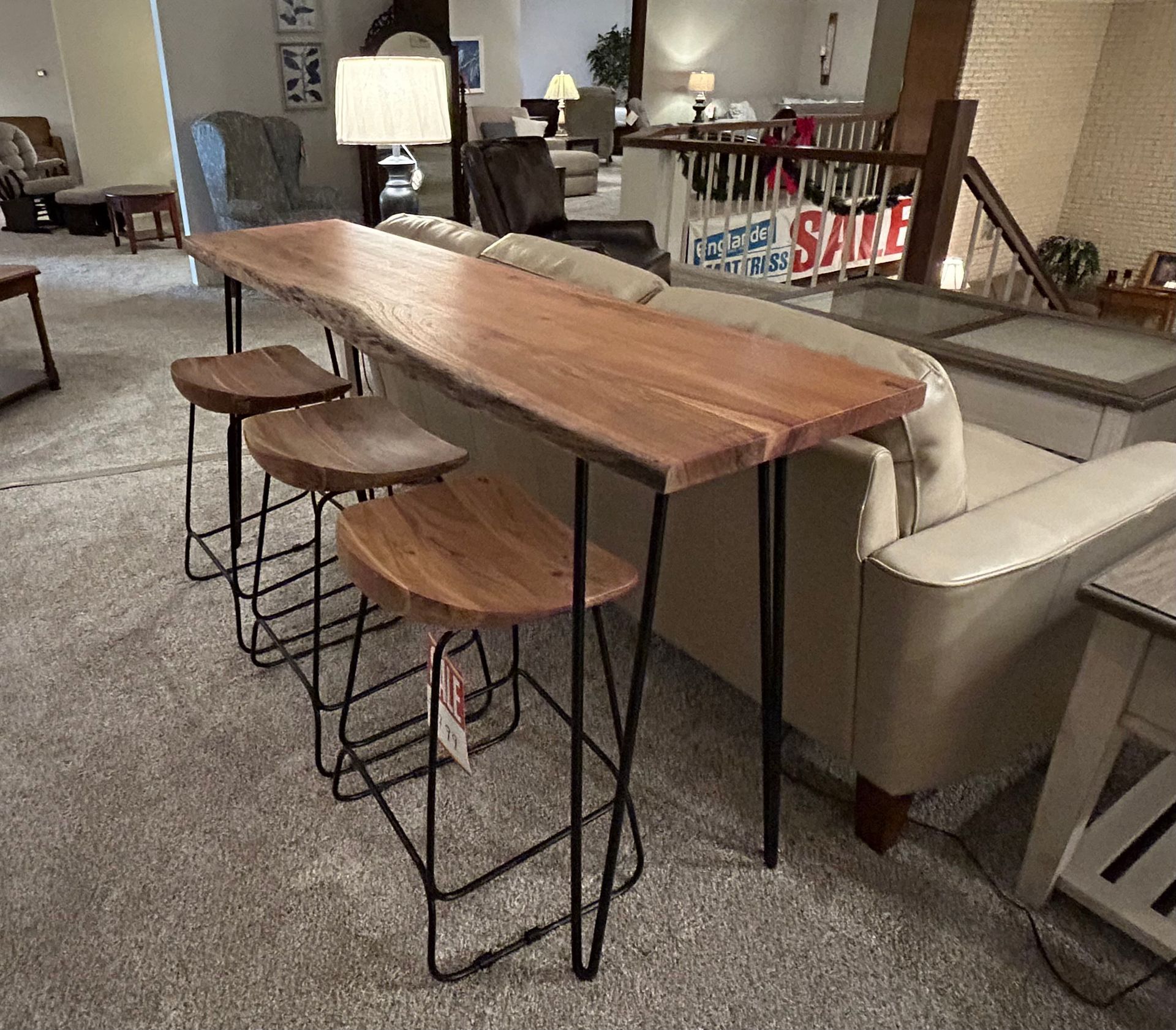Live-edge wood bar table with hairpin legs and three matching stools. Displayed in a furniture store setting.