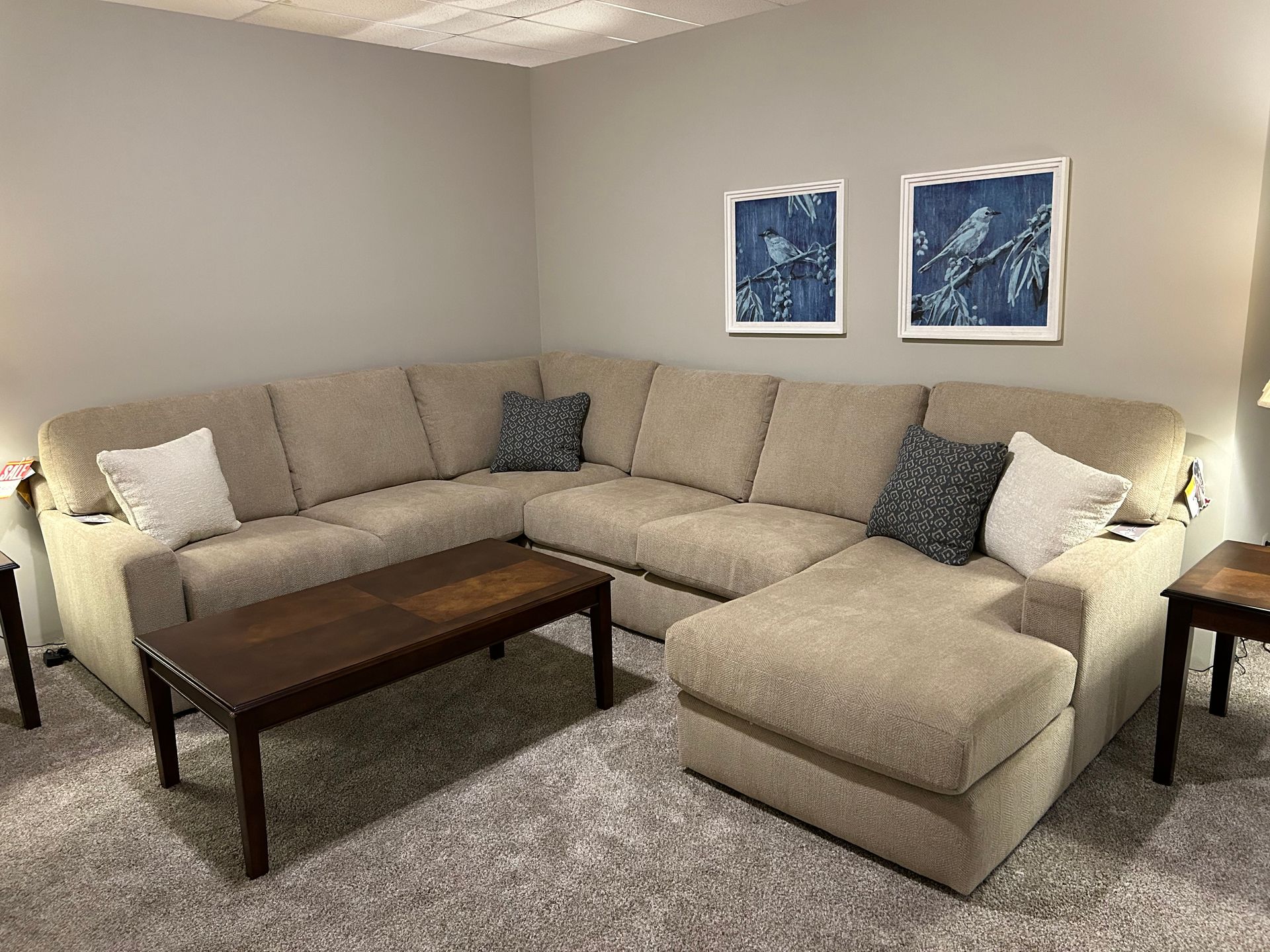 Beige sectional sofa in a living room with a brown coffee table and two framed blue prints.