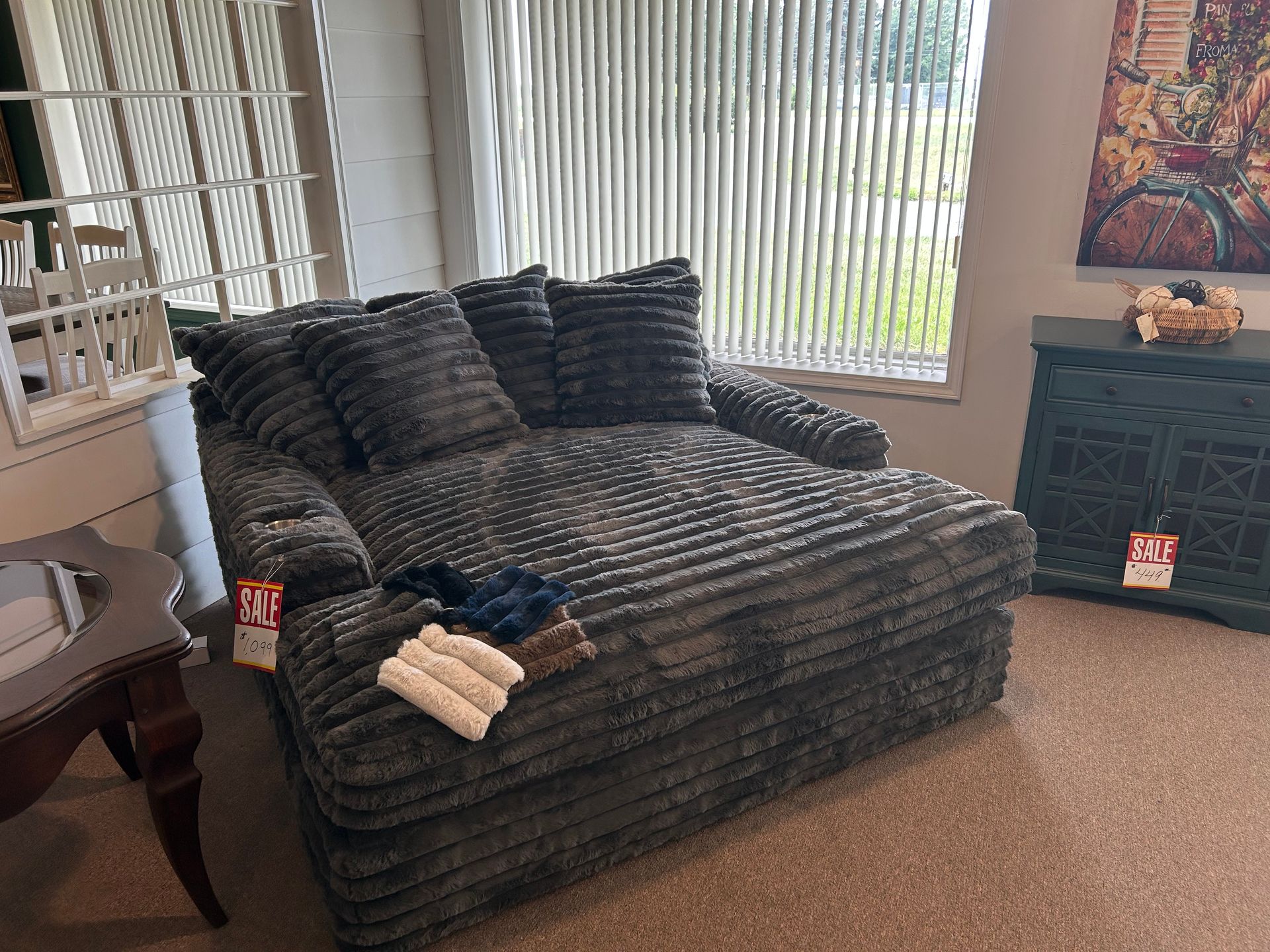 Gray corduroy chaise lounge with throw pillows near a window, with a side table and cabinet.