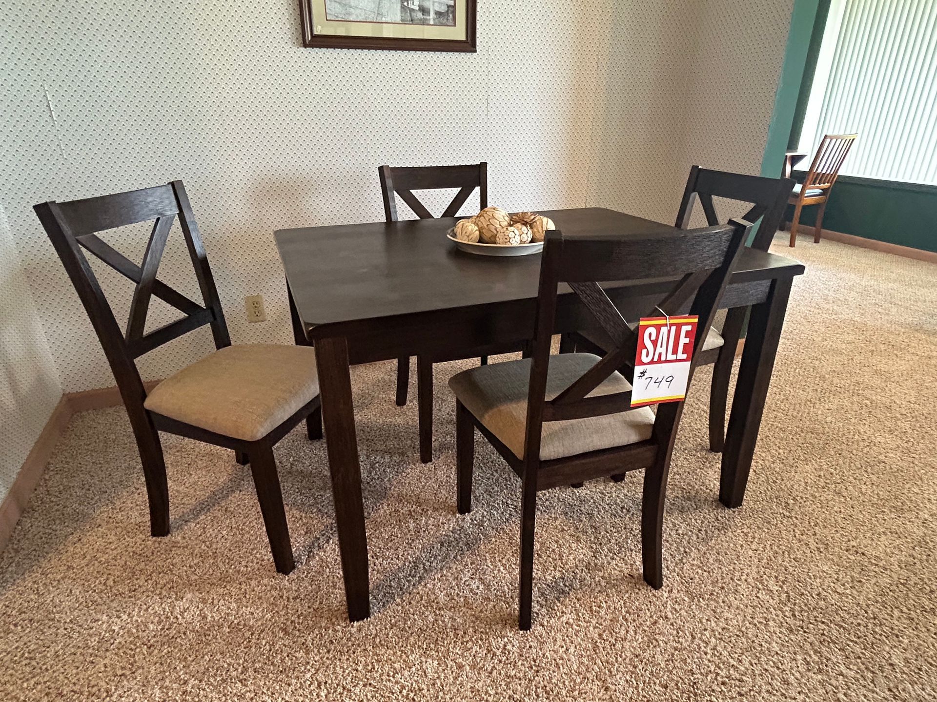 Dining table set with four chairs; dark wood, beige cushions, beige rug, and a sale tag.