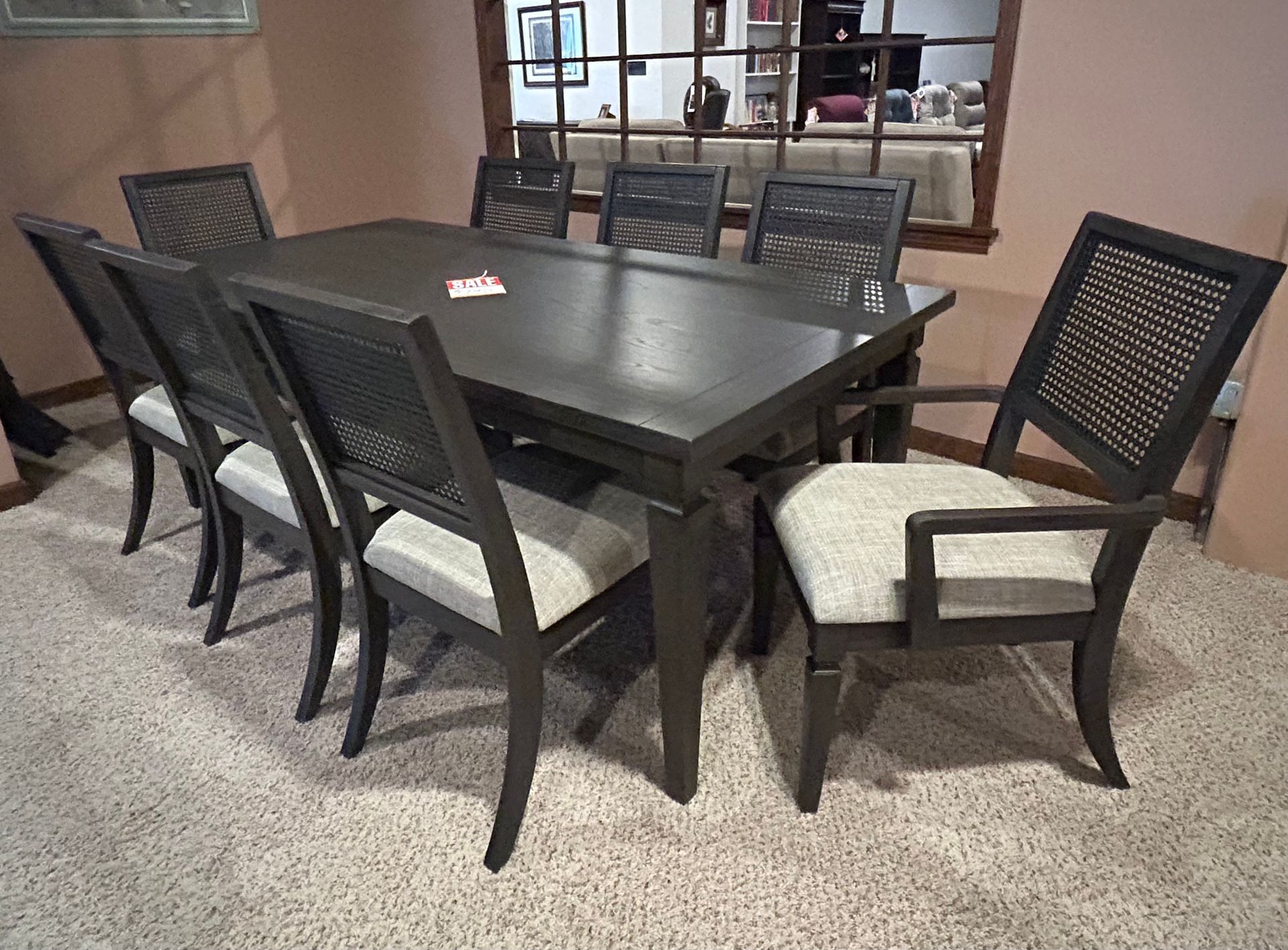 A dark wood dining table with eight chairs in a room with a mirror and speckled floor.