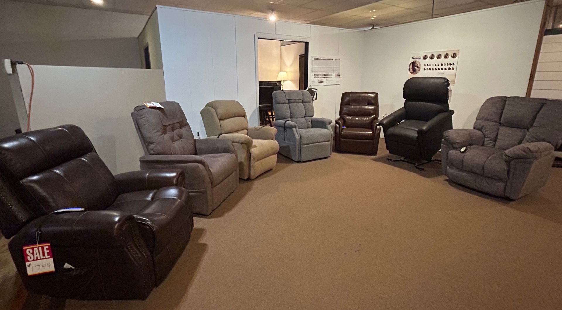 Recliner chairs in various colors displayed in a furniture store showroom on a brown carpet.