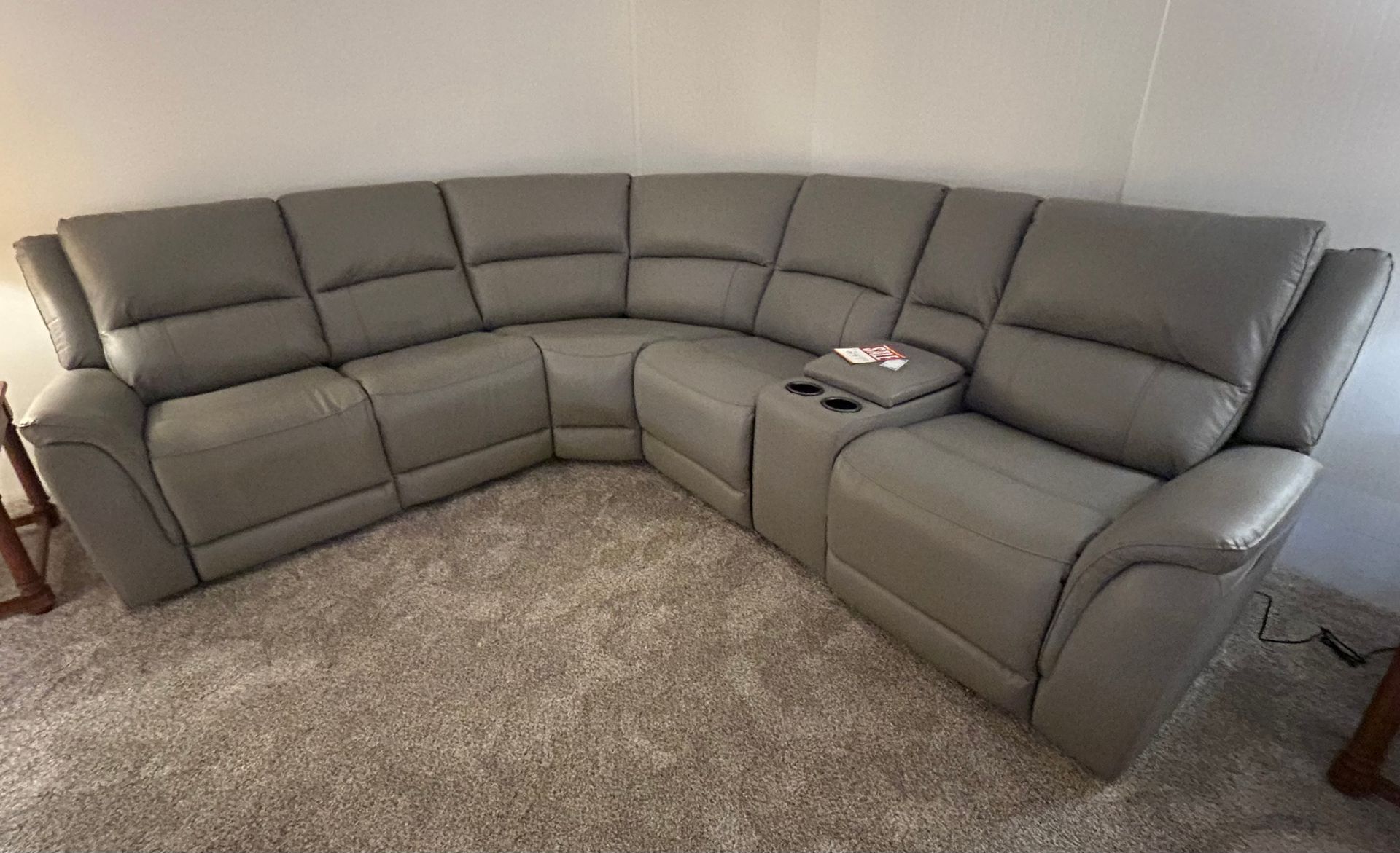 Gray leather sectional sofa with curved design and cup holders.