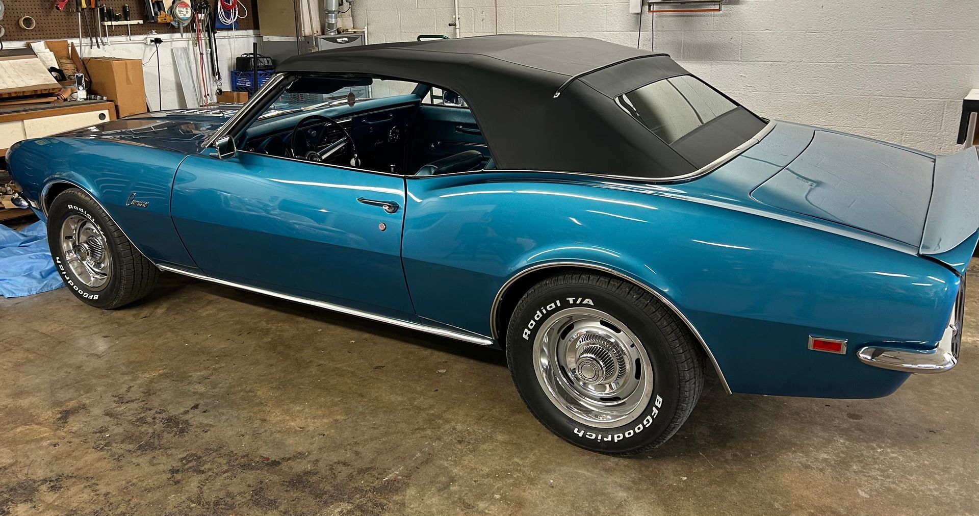 Teal convertible classic car with black top, parked indoors. Chrome wheels.