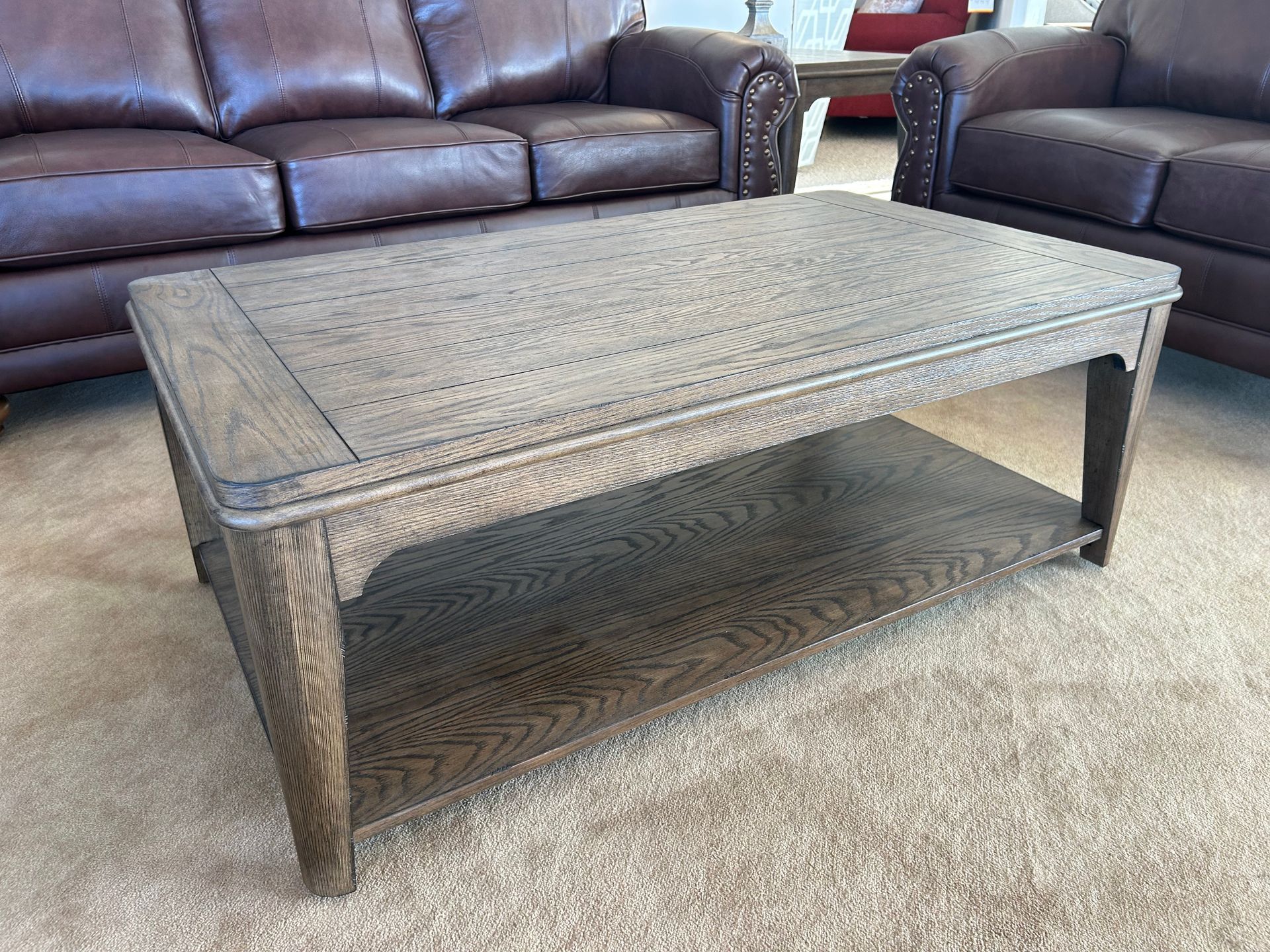 Wooden coffee table with an open shelf in front of a brown leather couch.