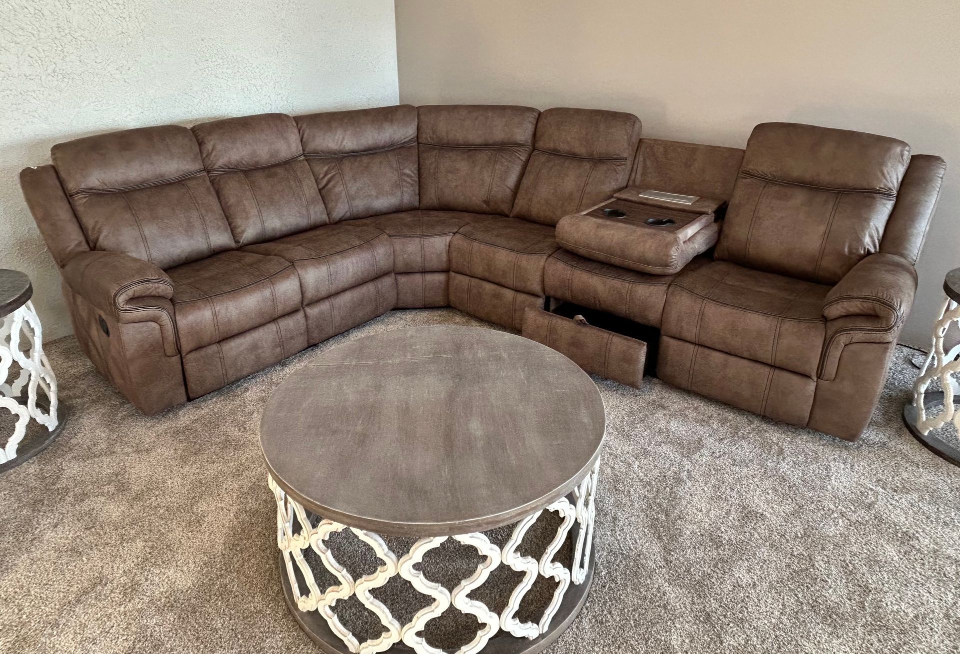 Brown leather sectional sofa with a center console and recliner, round coffee table on carpet.