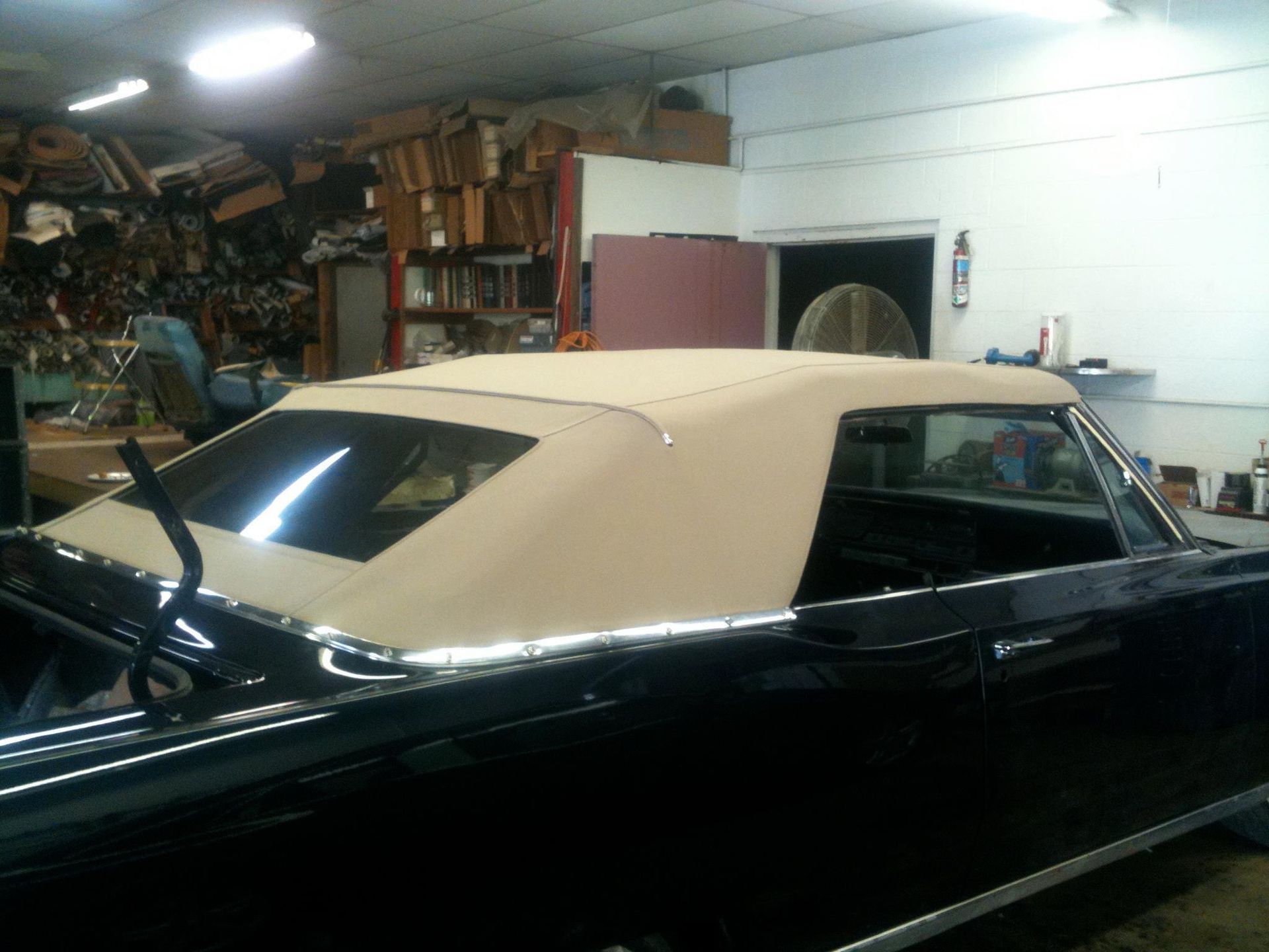 Black classic car with tan convertible top in a cluttered garage.