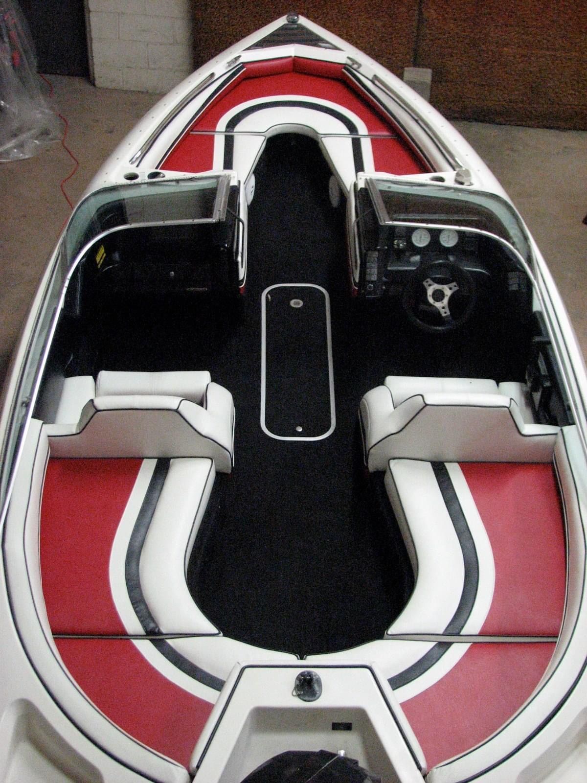 Boat interior with red and white seats, black carpet, and a steering wheel.