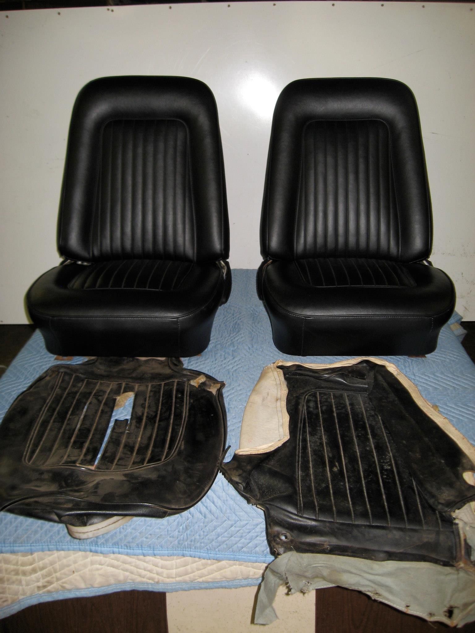 Two black car seats and two removed seat backs on a blue cloth.