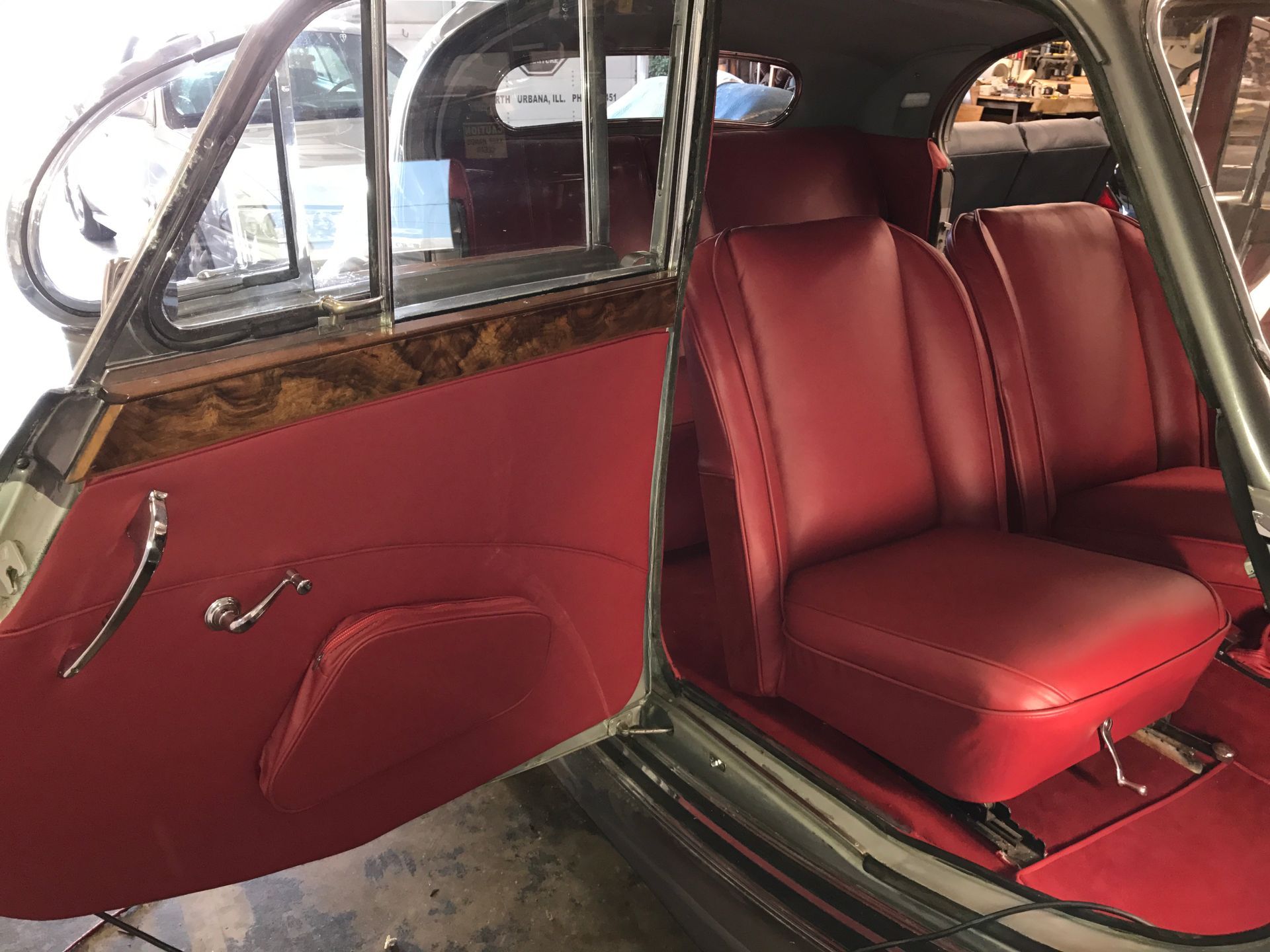 Interior of a classic car with red leather seats, door panel, and wood trim.