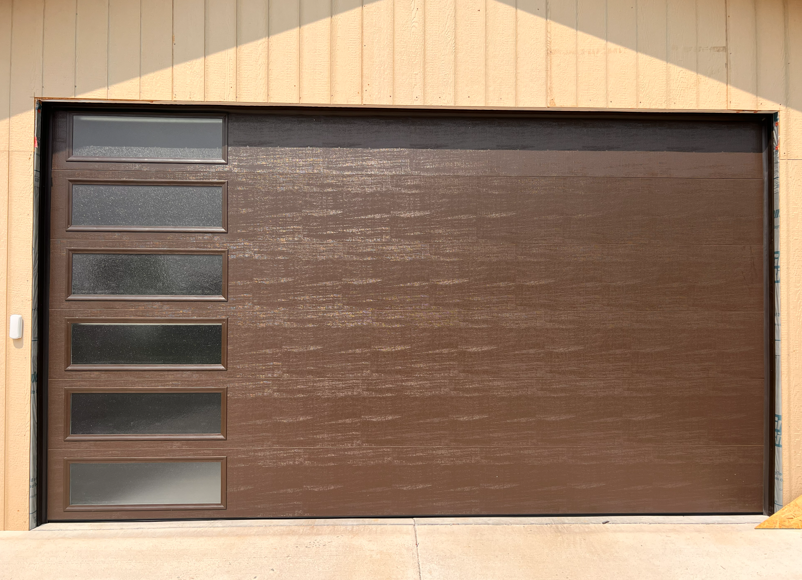 A brown horizontal-panel garage door featuring a vertical row of six rectangular frosted glass windows on the left.