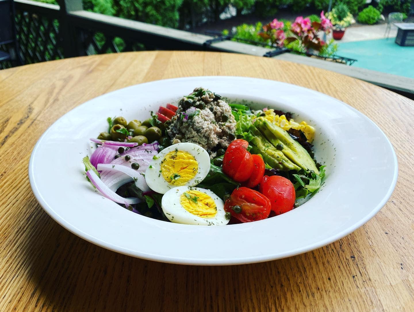 A bowl of salad with eggs tomatoes and avocado on a wooden table.