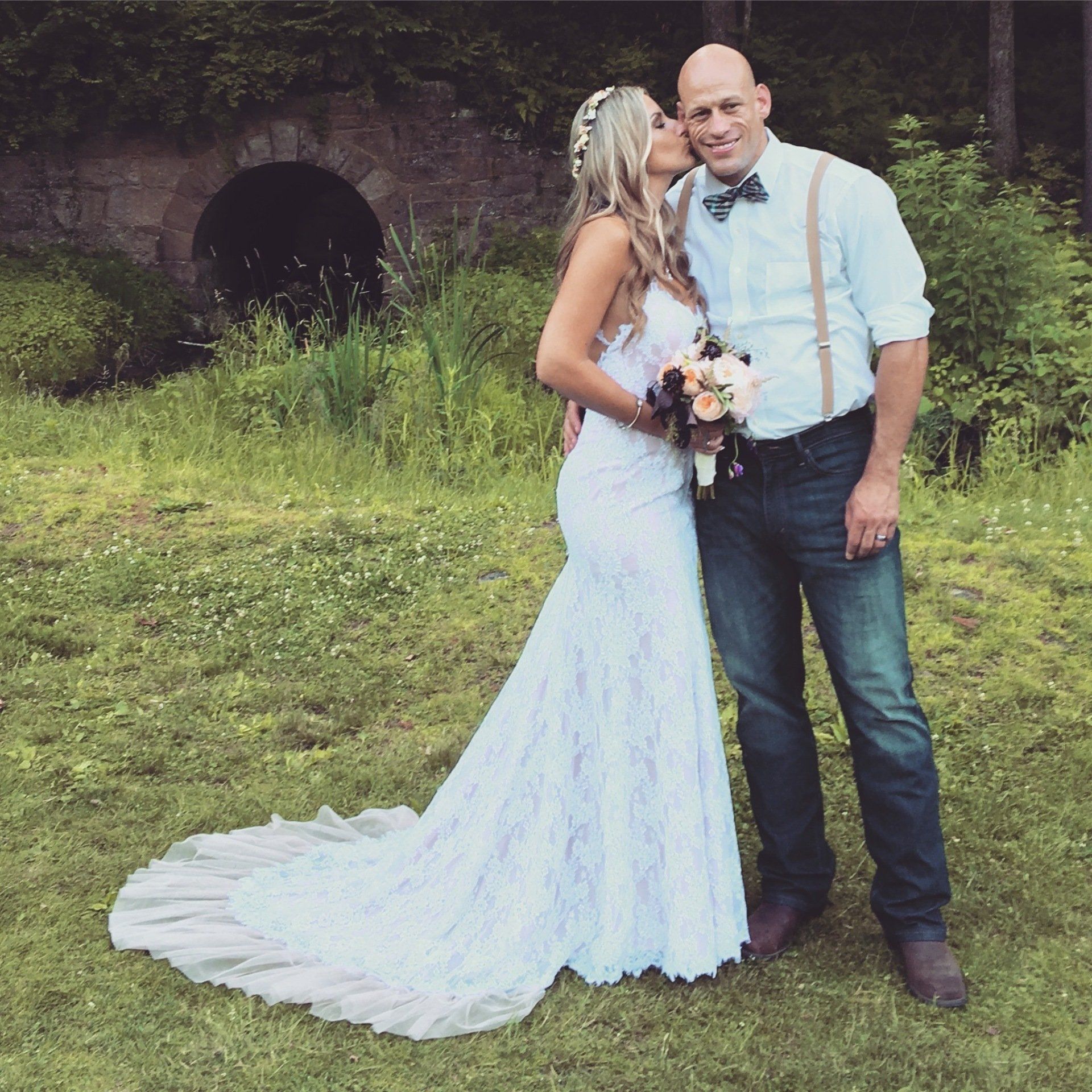A bride and groom pose for a picture in the grass