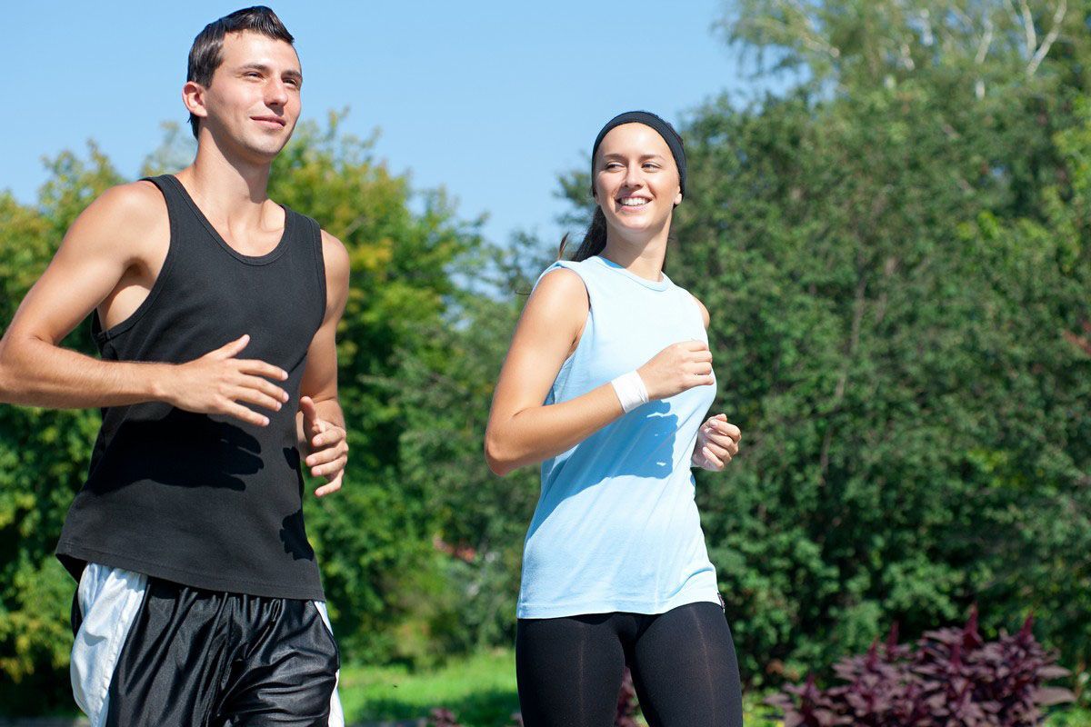 Two people jogging outdoors in athletic clothes on a sunny day