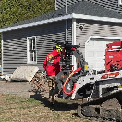 Man in red shirt operating a Bobcat with a wood chipper in front of a house.