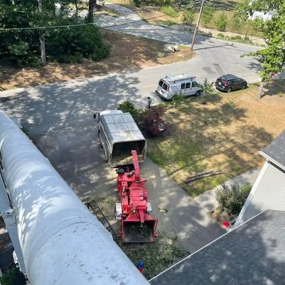 Aerial view: tree chipper in use, loading truck, man works outside, vehicles parked on street.