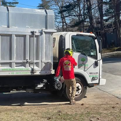 Man in red shirt near a white truck with a large metal container in a sunny outdoor setting.
