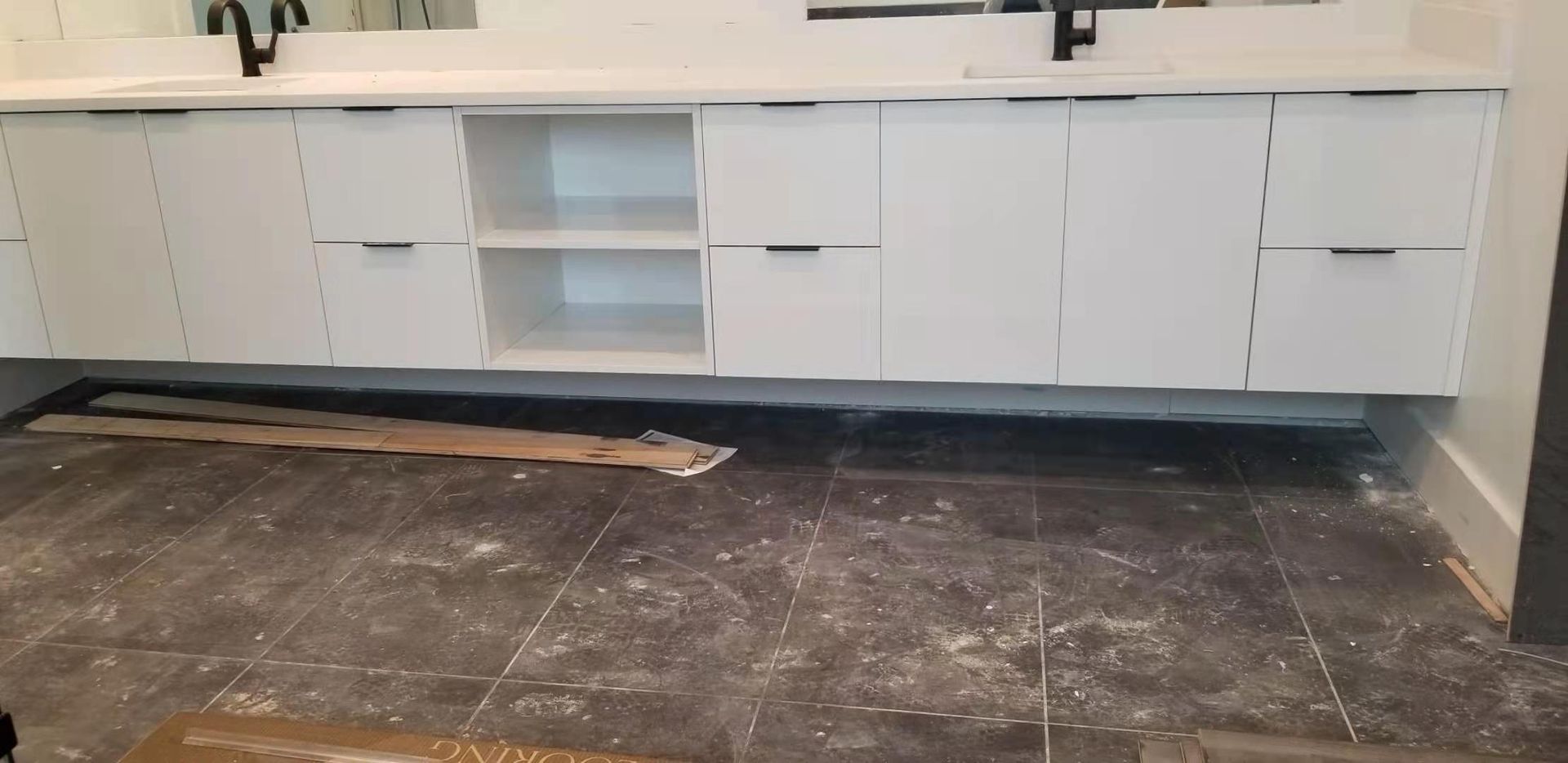 A bathroom with white cabinets and a black tile floor.