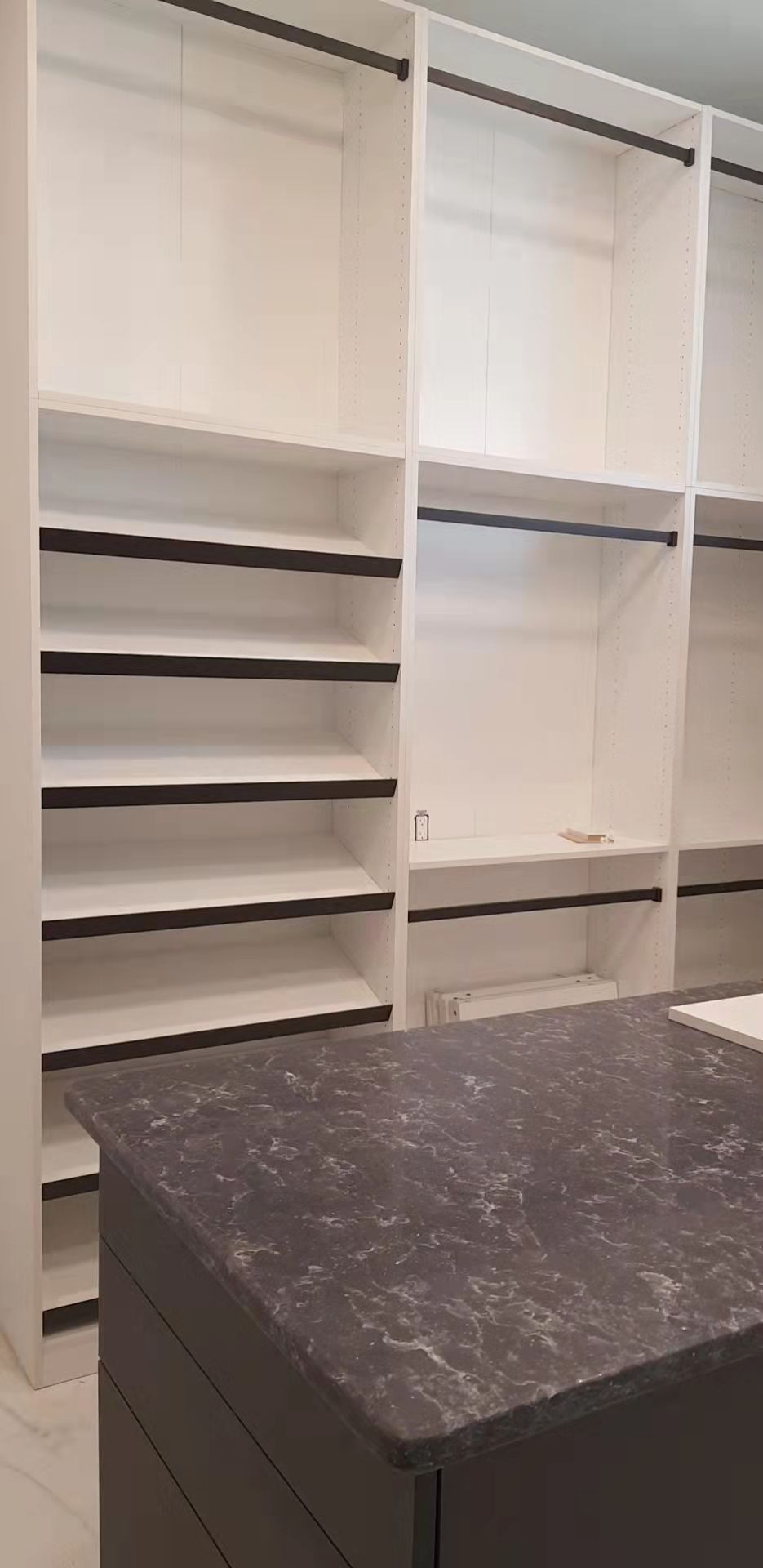 A walk in closet with white shelves and a black counter top.