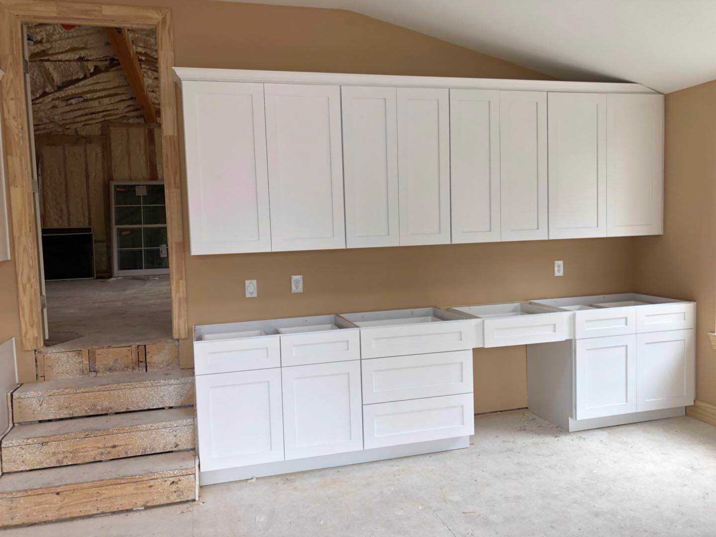 A kitchen under construction with white cabinets and marble counter tops.