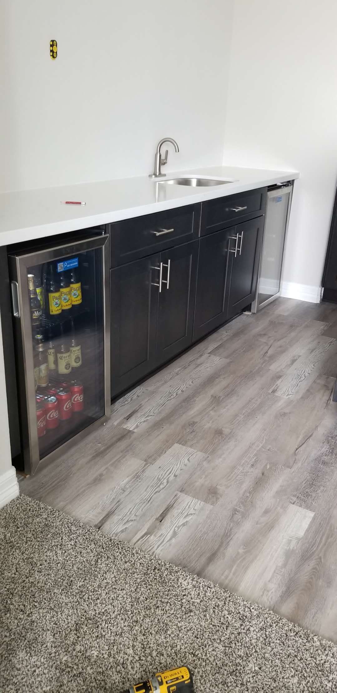 A kitchen with black cabinets , a sink , and a refrigerator.