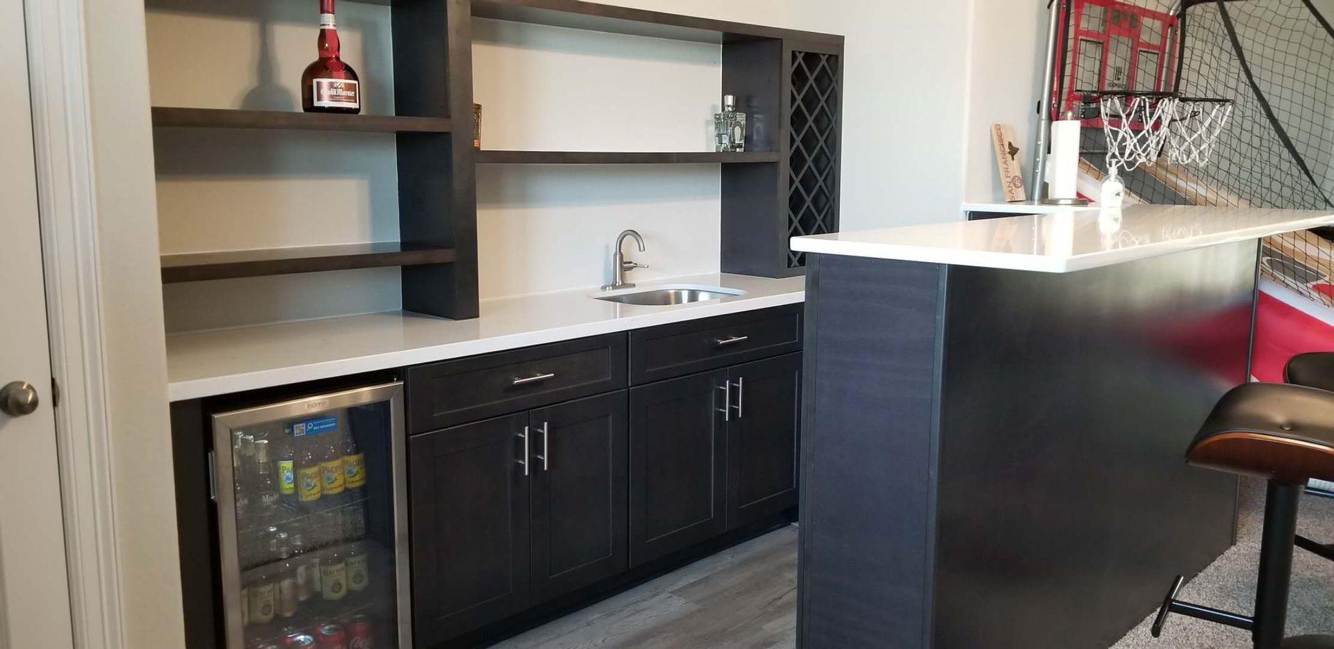 A kitchen with a bar , sink , refrigerator and shelves.