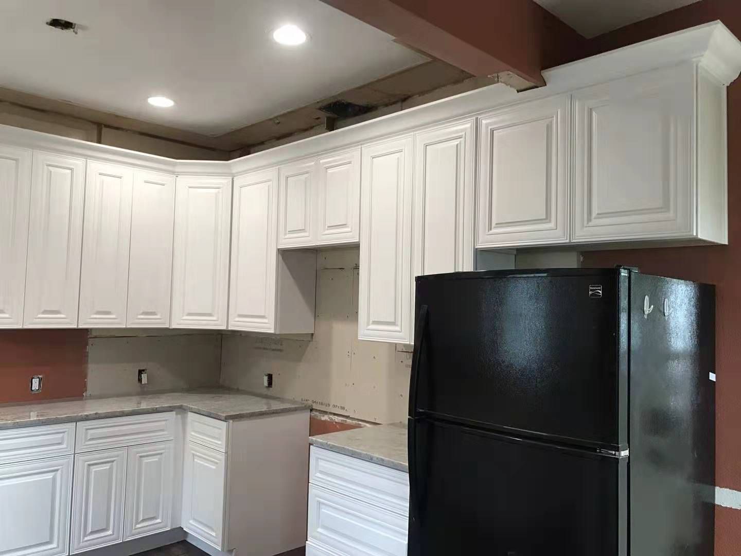 A kitchen with white cabinets and a black refrigerator.
