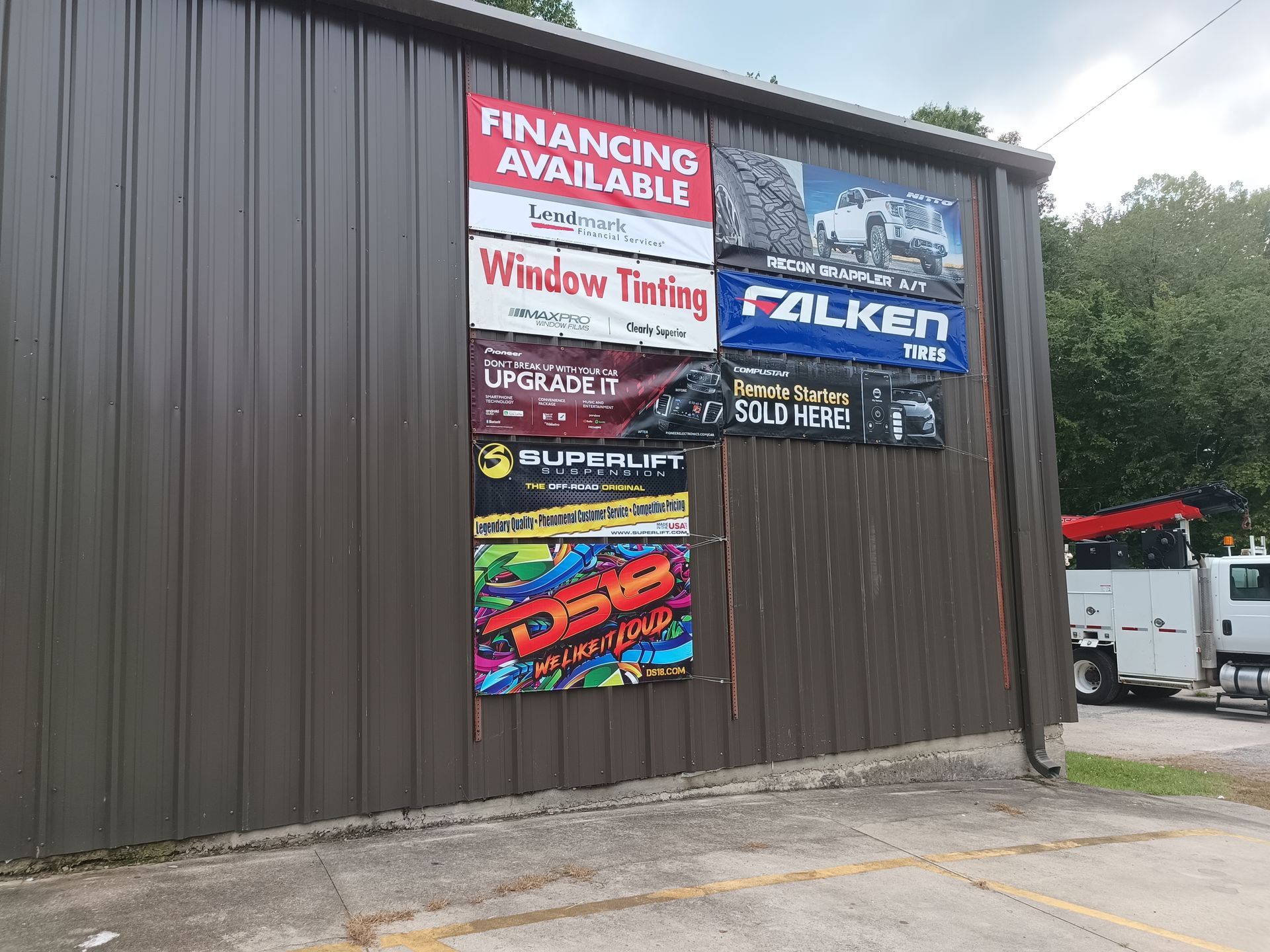 Signs on a brown building: Financing, window tinting, tire brands, and a colorful advertisement.