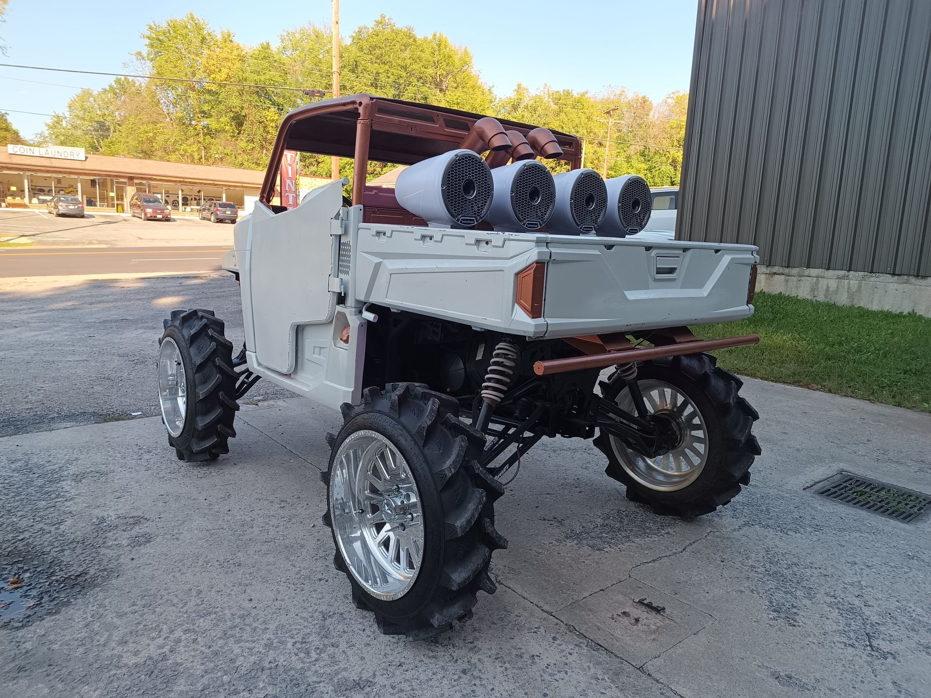 White off-road vehicle with large mud tires, silver wheels, and speakers mounted on the rear.