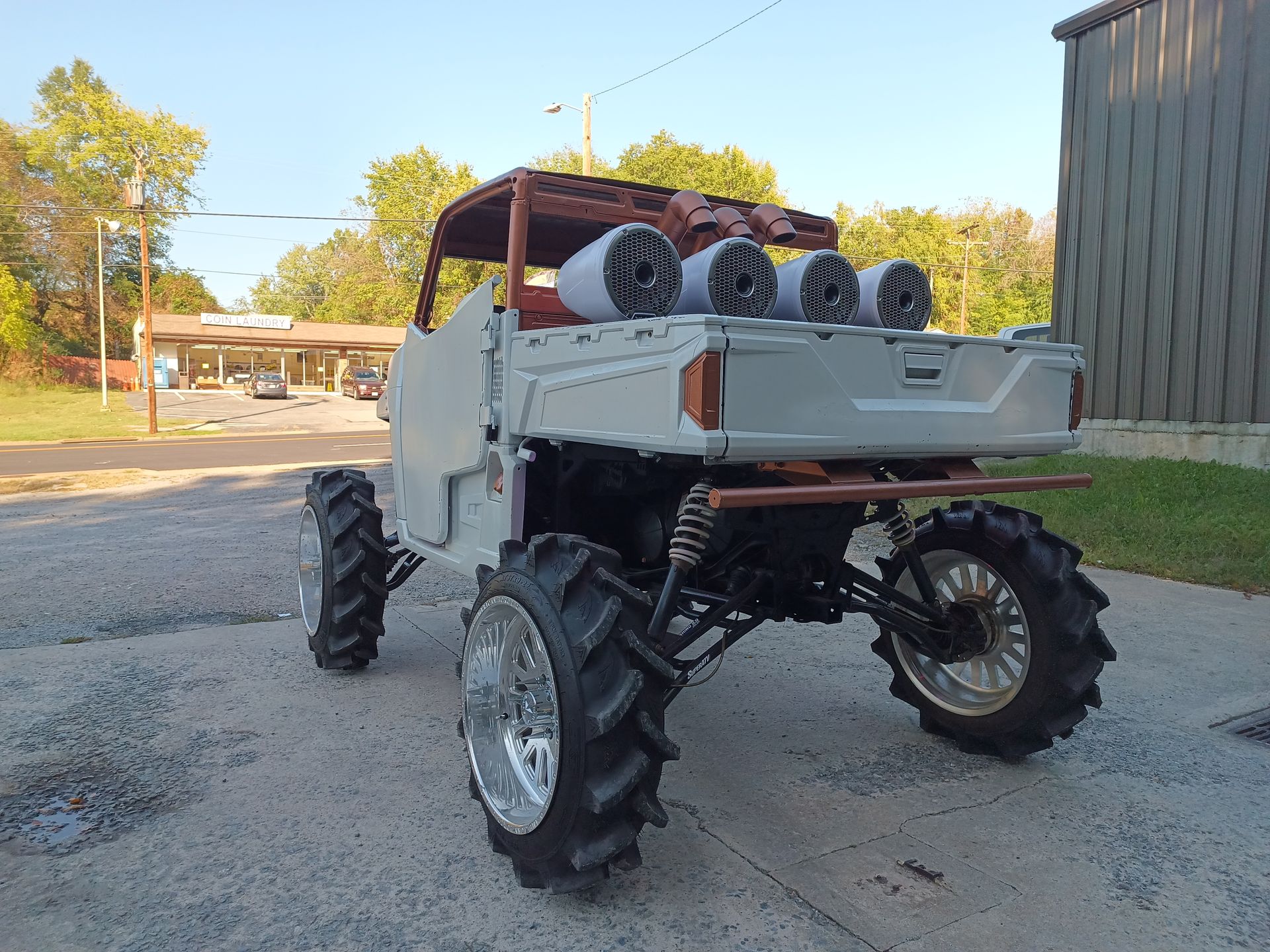 Modified off-road vehicle with large tires, four exhaust stacks, and a roll cage, parked outside.