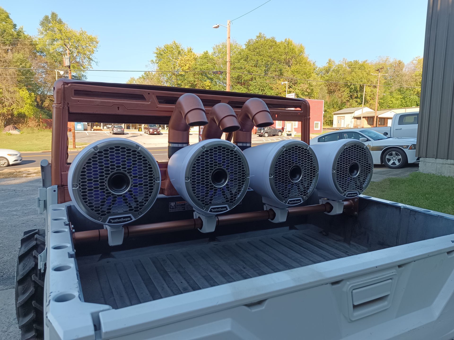 White truck bed with four large speakers mounted on a copper frame.