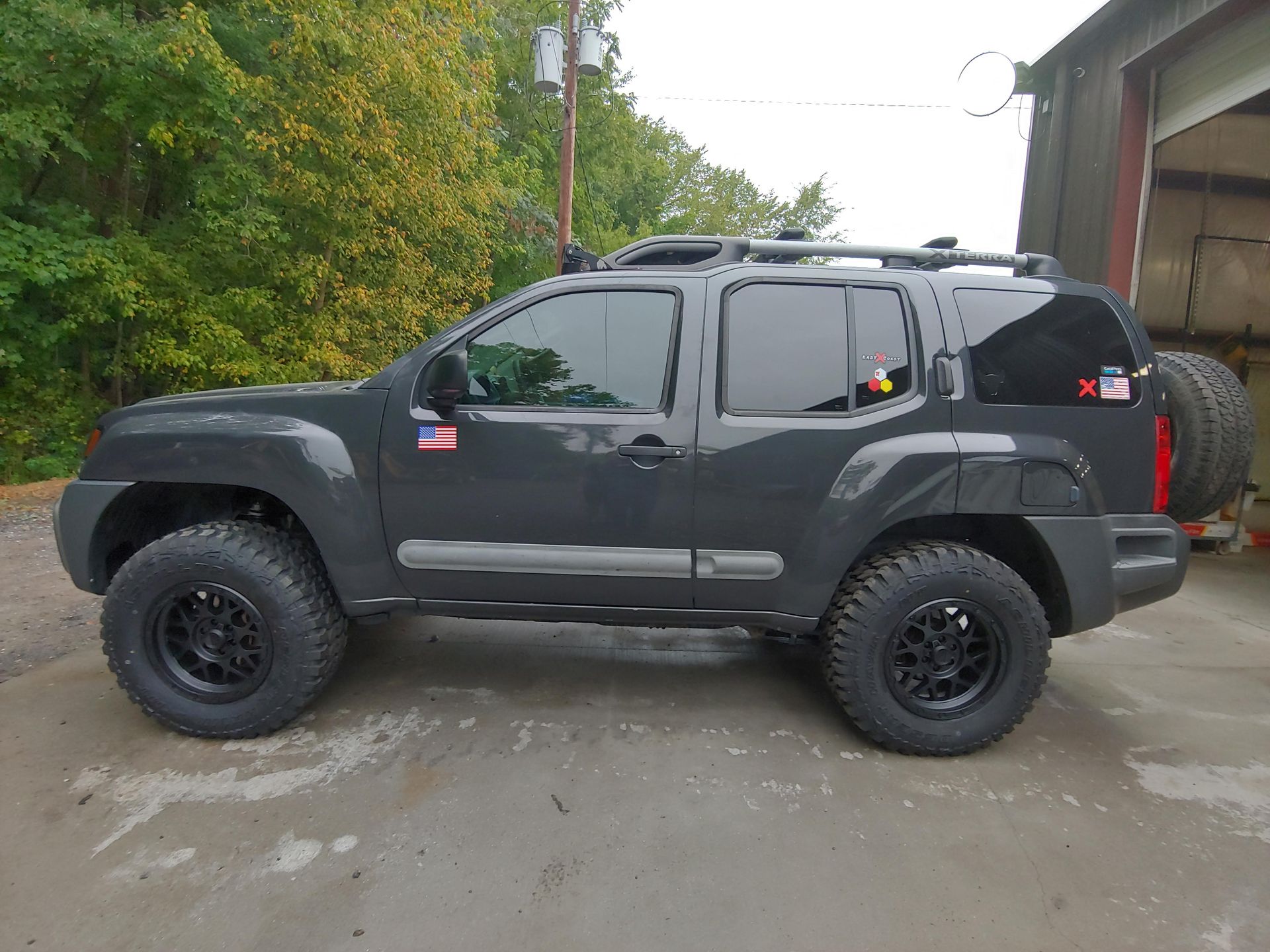Dark gray Nissan Xterra SUV with black wheels and spare tire on the back. It is parked outside.