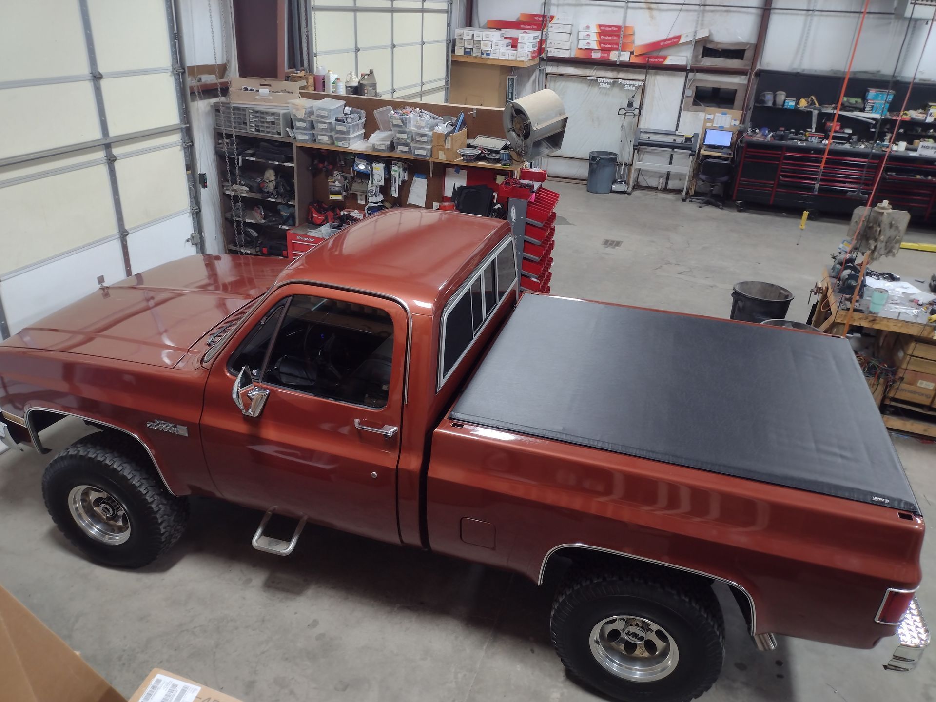 Brown pickup truck inside a garage, viewed from above. It has a black tonneau cover and chrome accents.