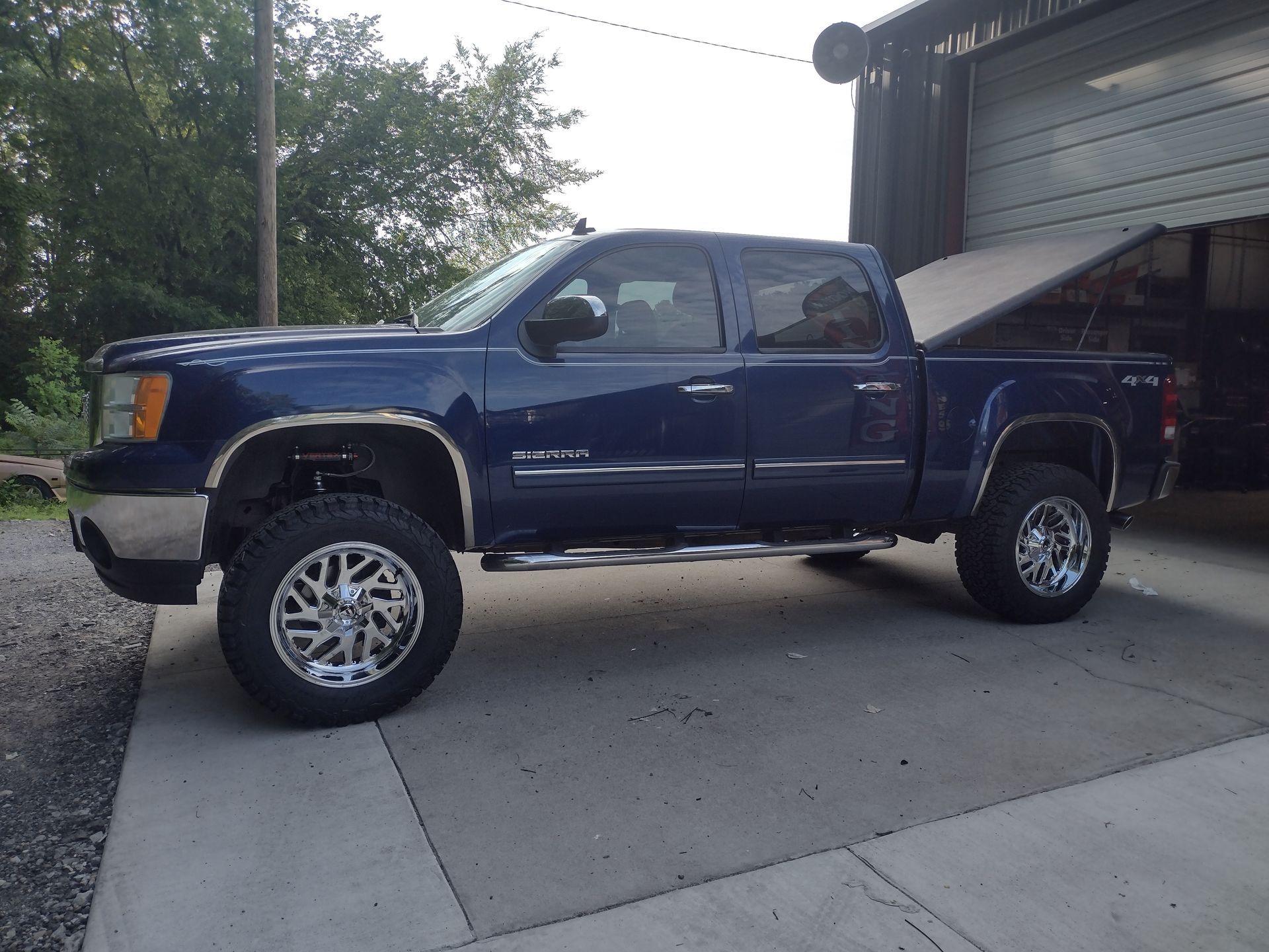 Dark blue lifted pickup truck with chrome accents and large wheels parked in front of a garage.