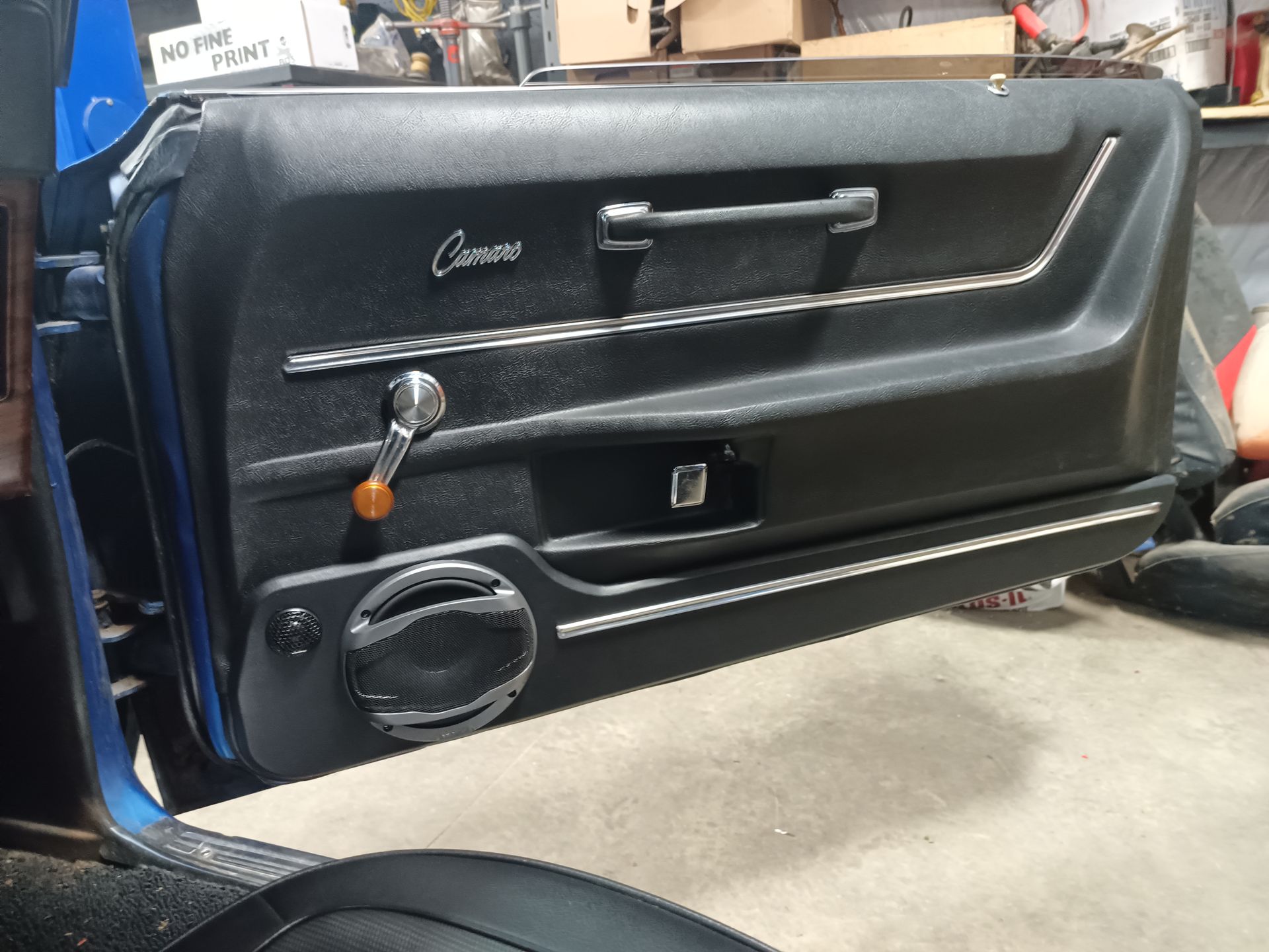 Black car door panel with speaker, chrome handle, and Camaro emblem.