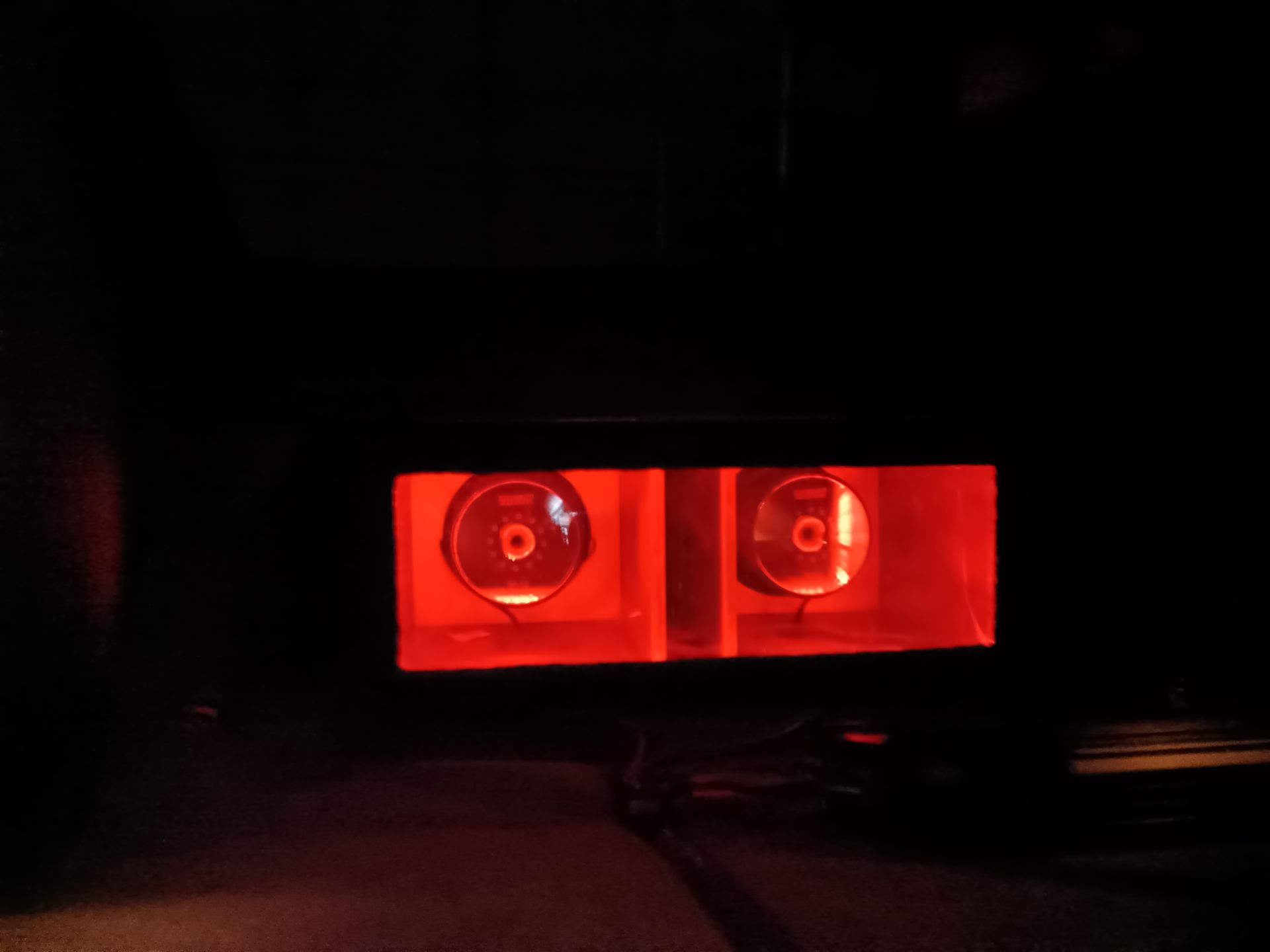 Two red-lit speakers within a dark enclosure.