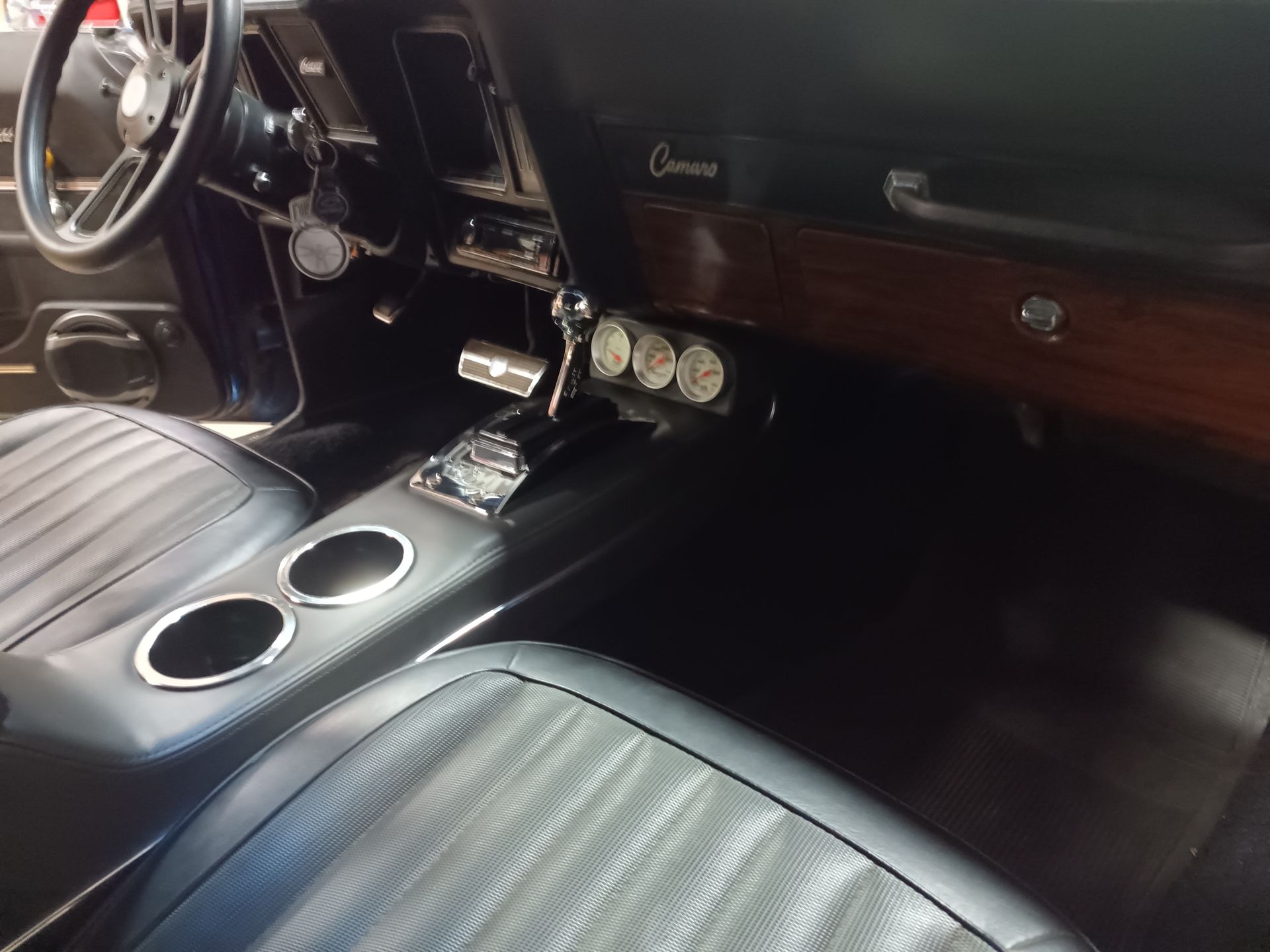 Interior of a classic black Camaro. Shows seats, dashboard, gauges, console, and steering wheel.