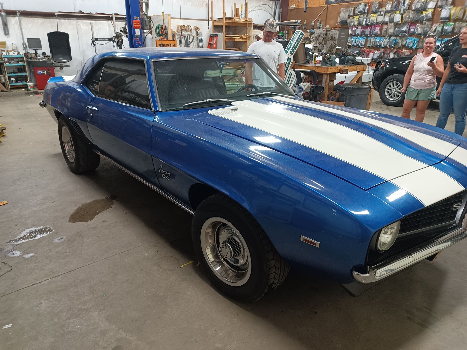 Blue classic car with white racing stripes in a workshop.
