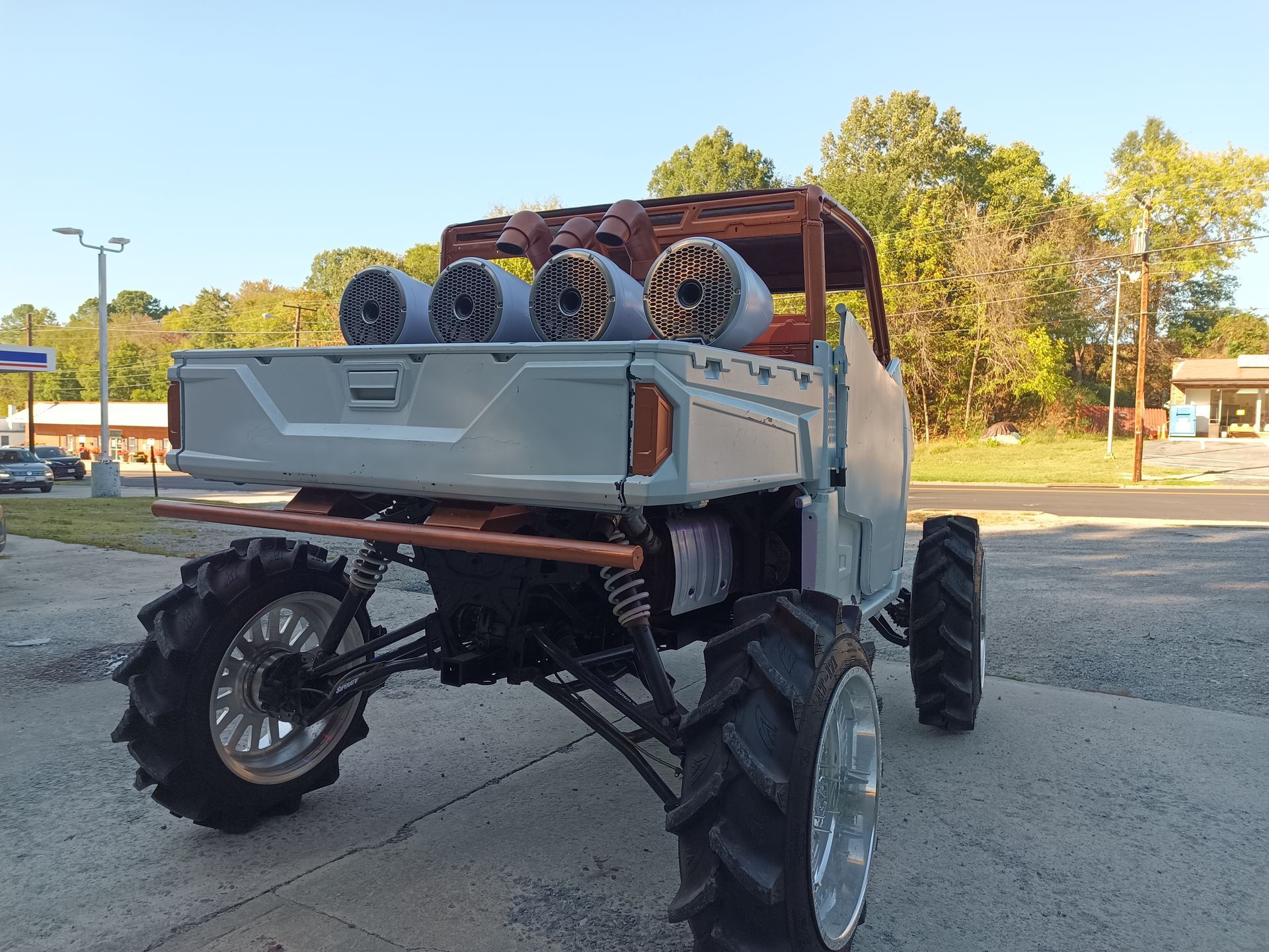Modified gray off-road vehicle with large tires, four speakers, and wooden roof.