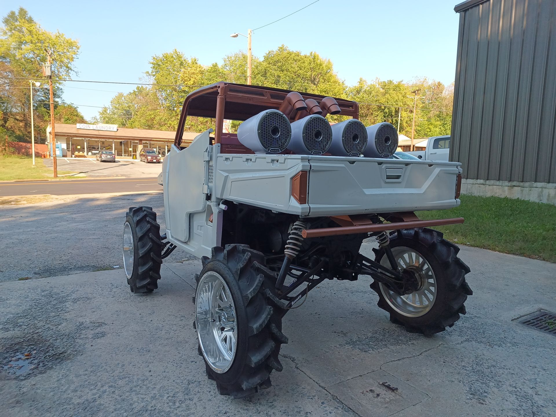 Mud-tire ATV with custom speaker system and roll cage, parked outside near a building.
