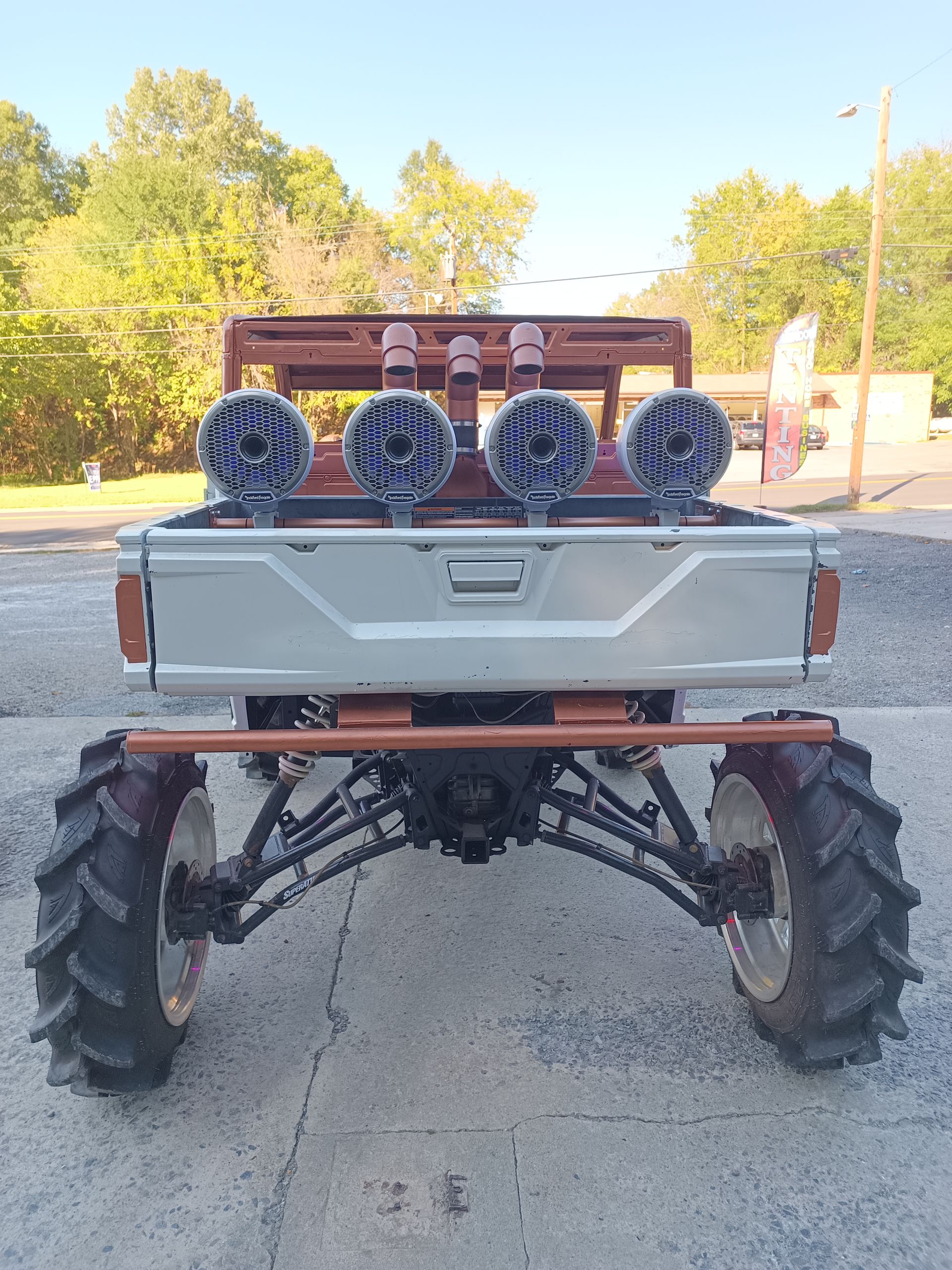 Rear view of a mud truck, with large tires, four lights on the bed, and a brown frame.