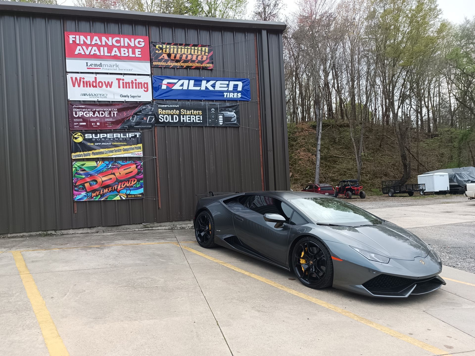 Gray Lamborghini parked in front of a building with signs for financing, window tinting, and tires.